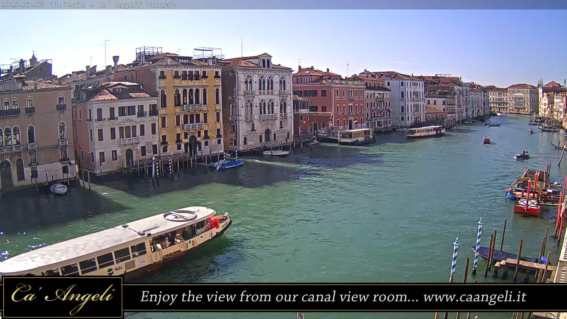 A sunny day in Venice shows a wide canal with many boats and colorful buildings lining the waterway.