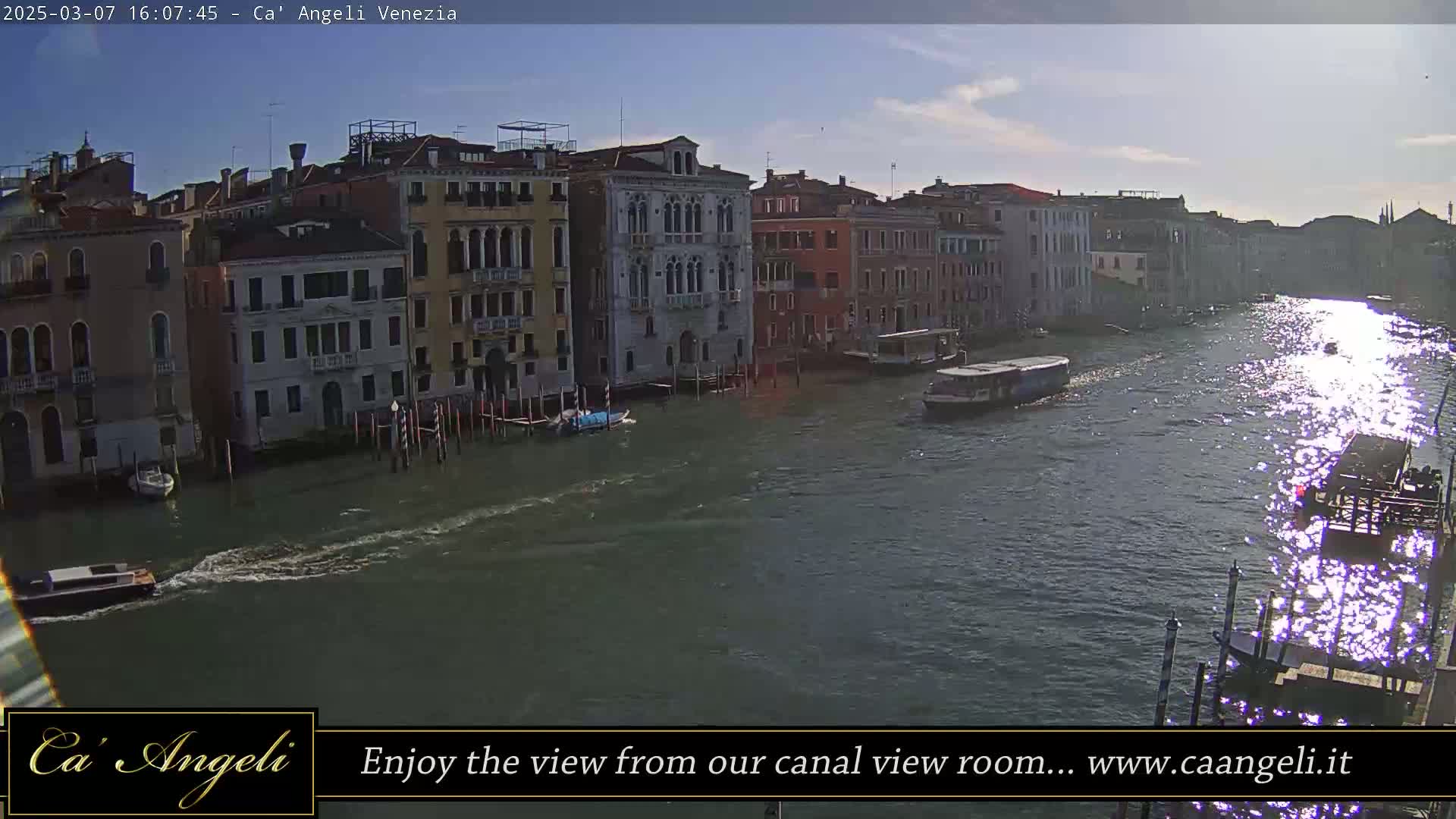 A sunny day in Venice shows a canal with several boats, lined with historic buildings on either side.