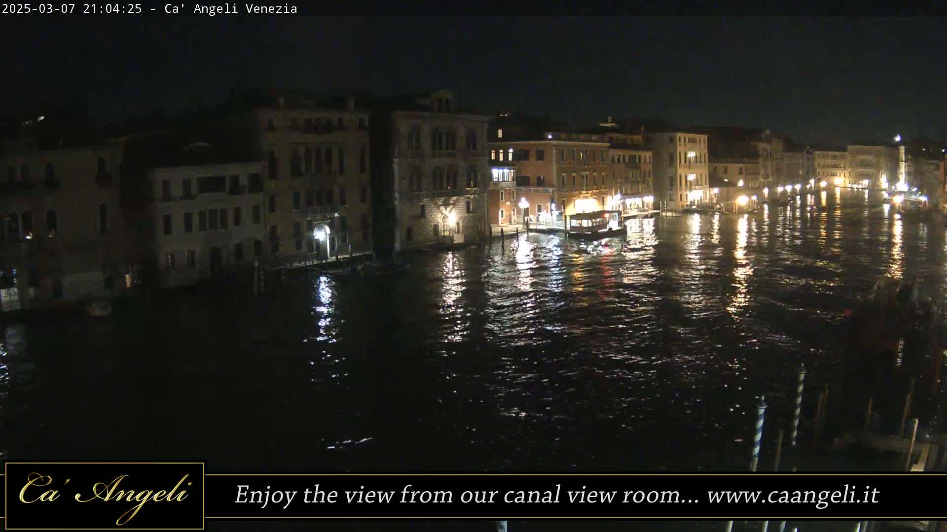 A nighttime view of a canal in Venice, with lights reflecting on the water and buildings lining the waterway.