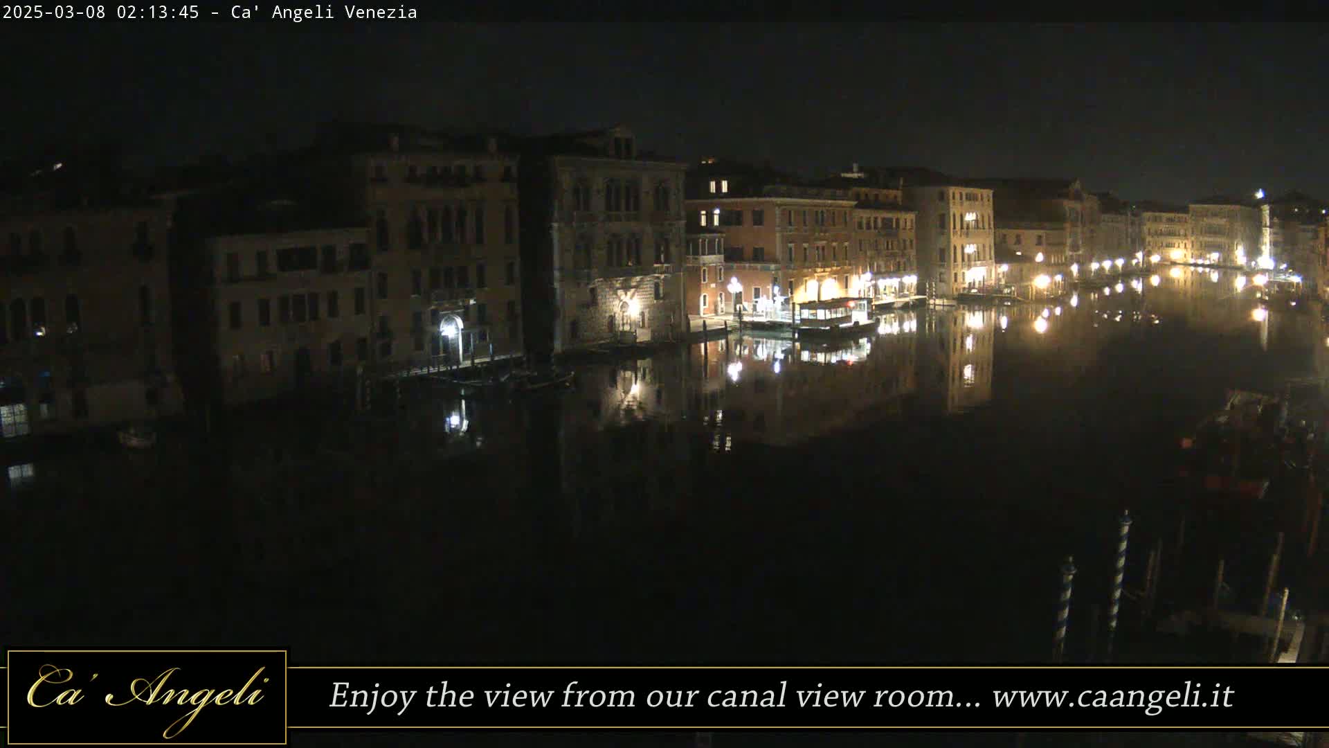 A nighttime view of a canal in Venice, showing illuminated buildings reflected in the dark water.