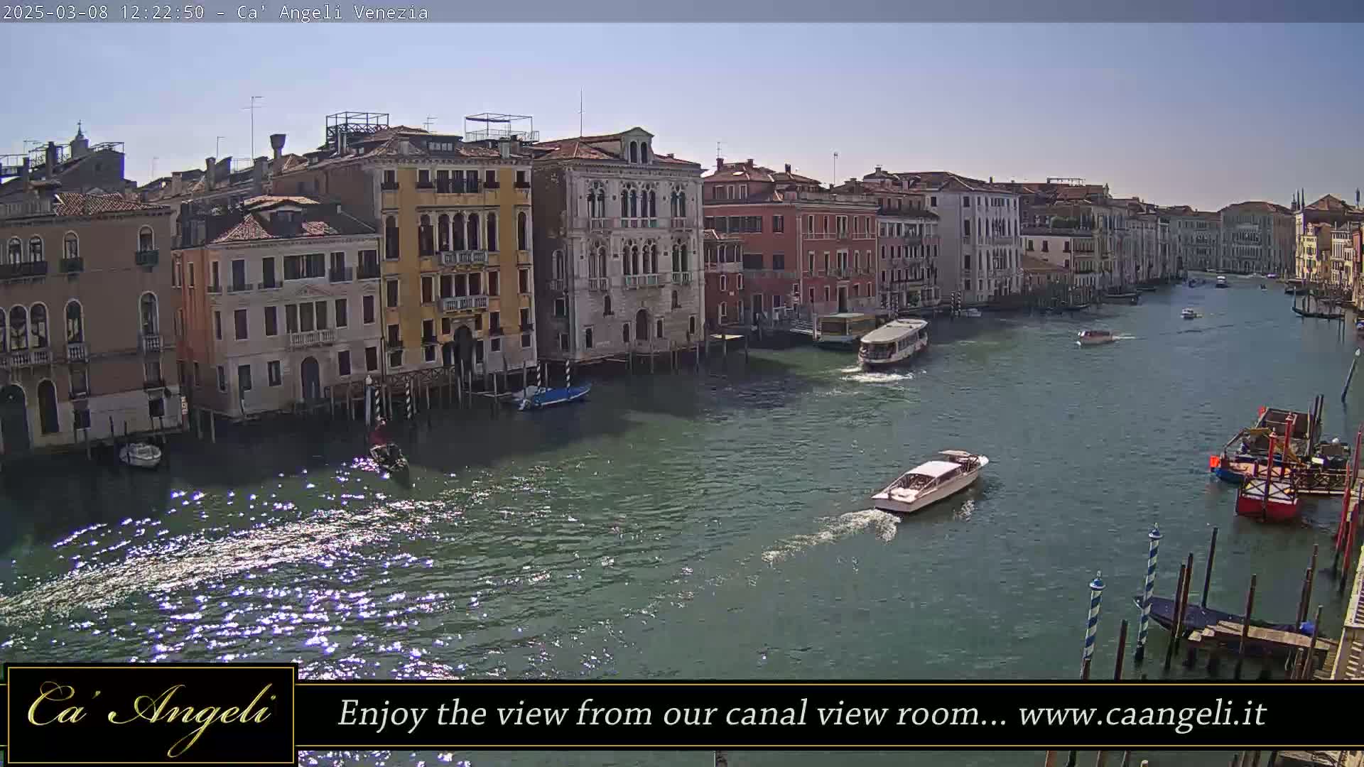 A sunny day in Venice shows several boats on a canal lined with tall, colorful buildings.