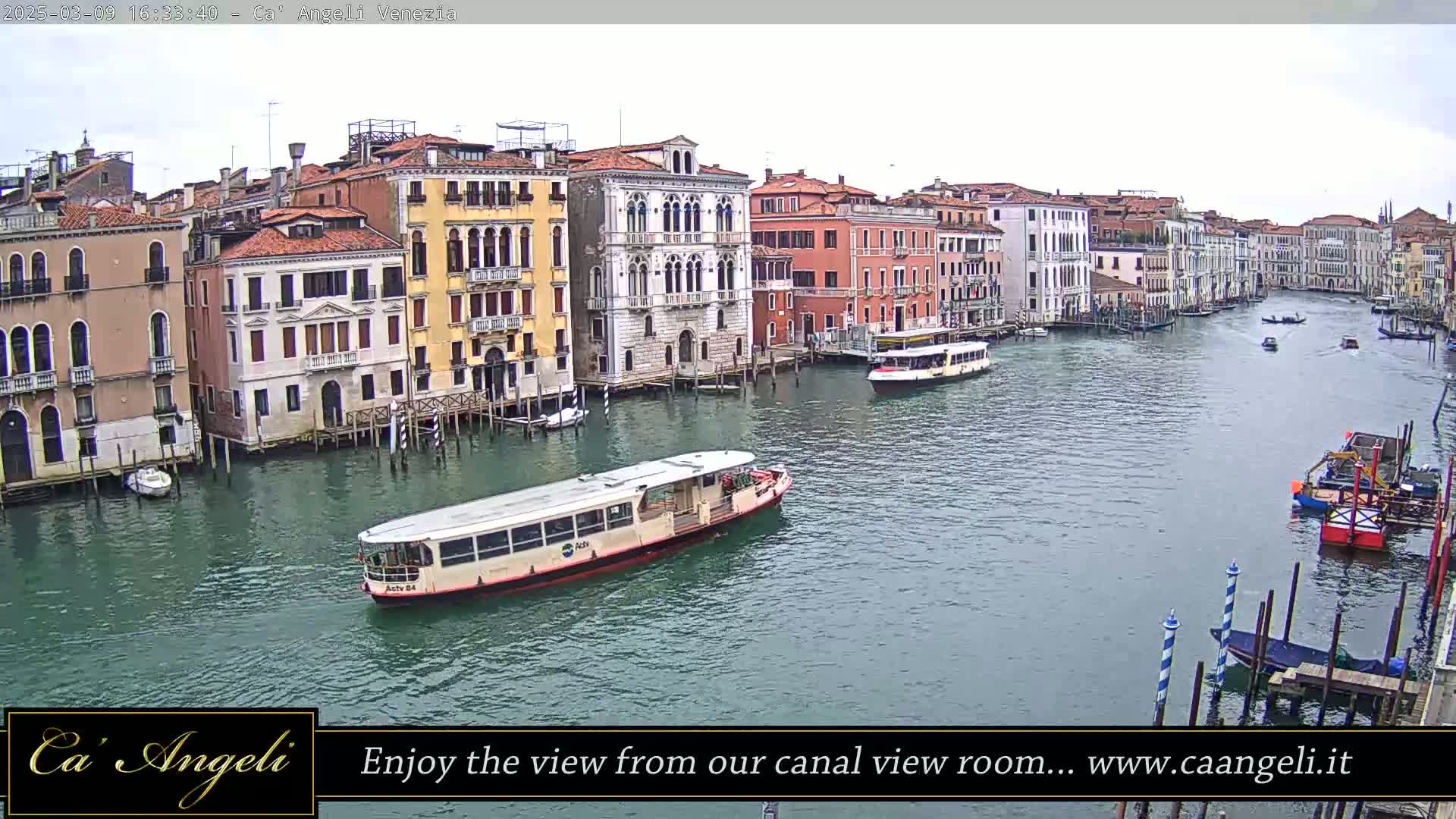 A waterway in Venice, under an overcast sky, is filled with boats and lined with colorful buildings.
