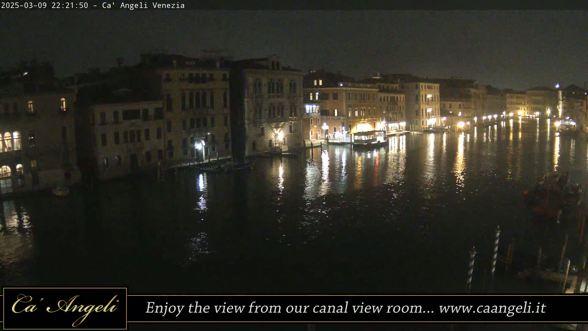 A nighttime view of a canal in Venice, showing illuminated buildings lining the waterway, with calm water reflecting the lights.