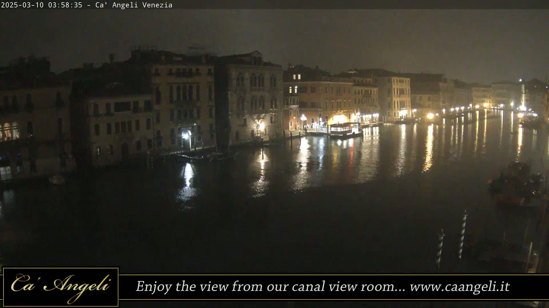 A nighttime view of a canal in Venice, with buildings lining the waterway under a dark, possibly rainy sky.