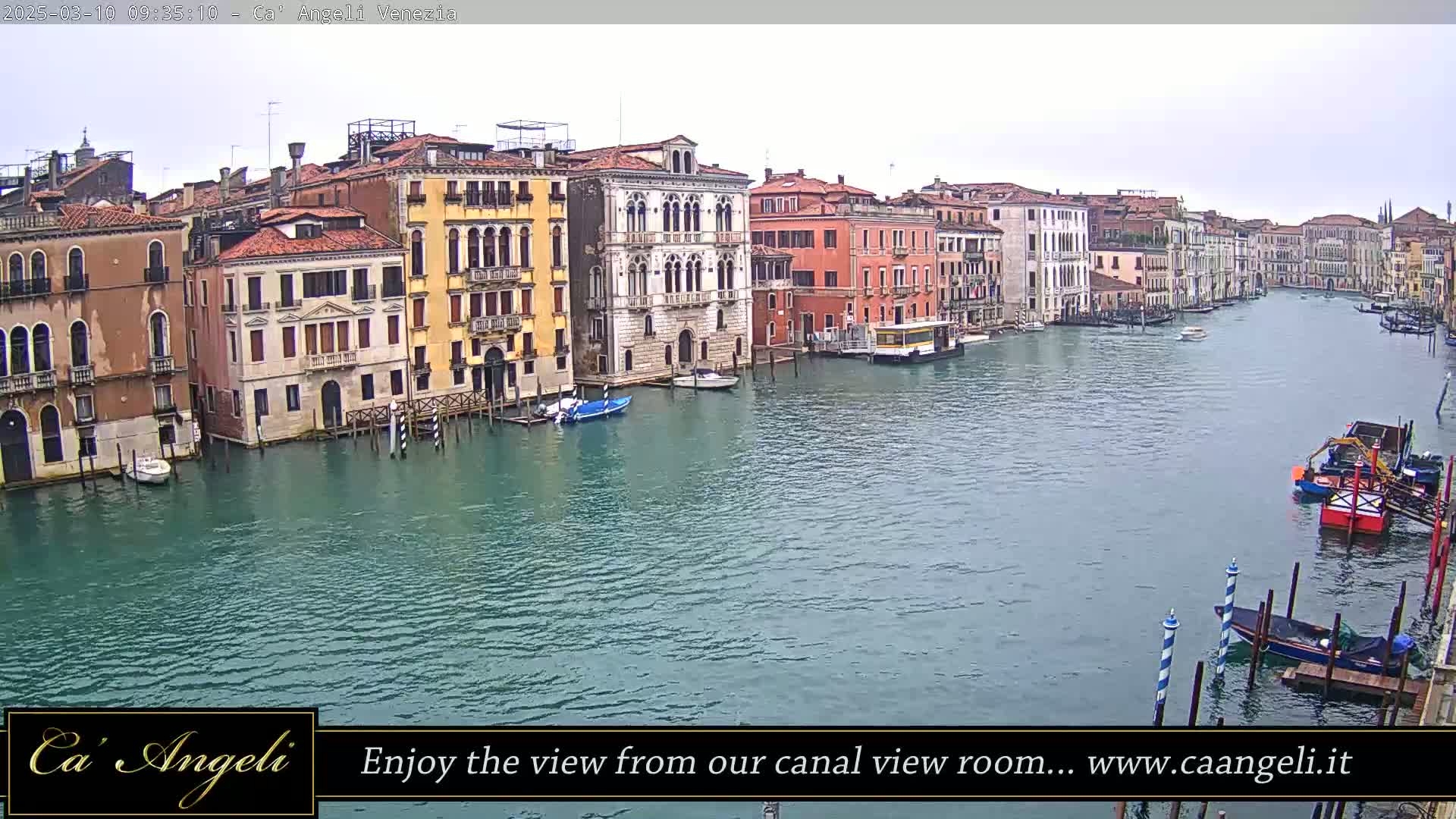 A wide shot of a waterway in Venice, Italy, on an overcast day, shows multiple buildings lining the canal with several boats moored along the sides.