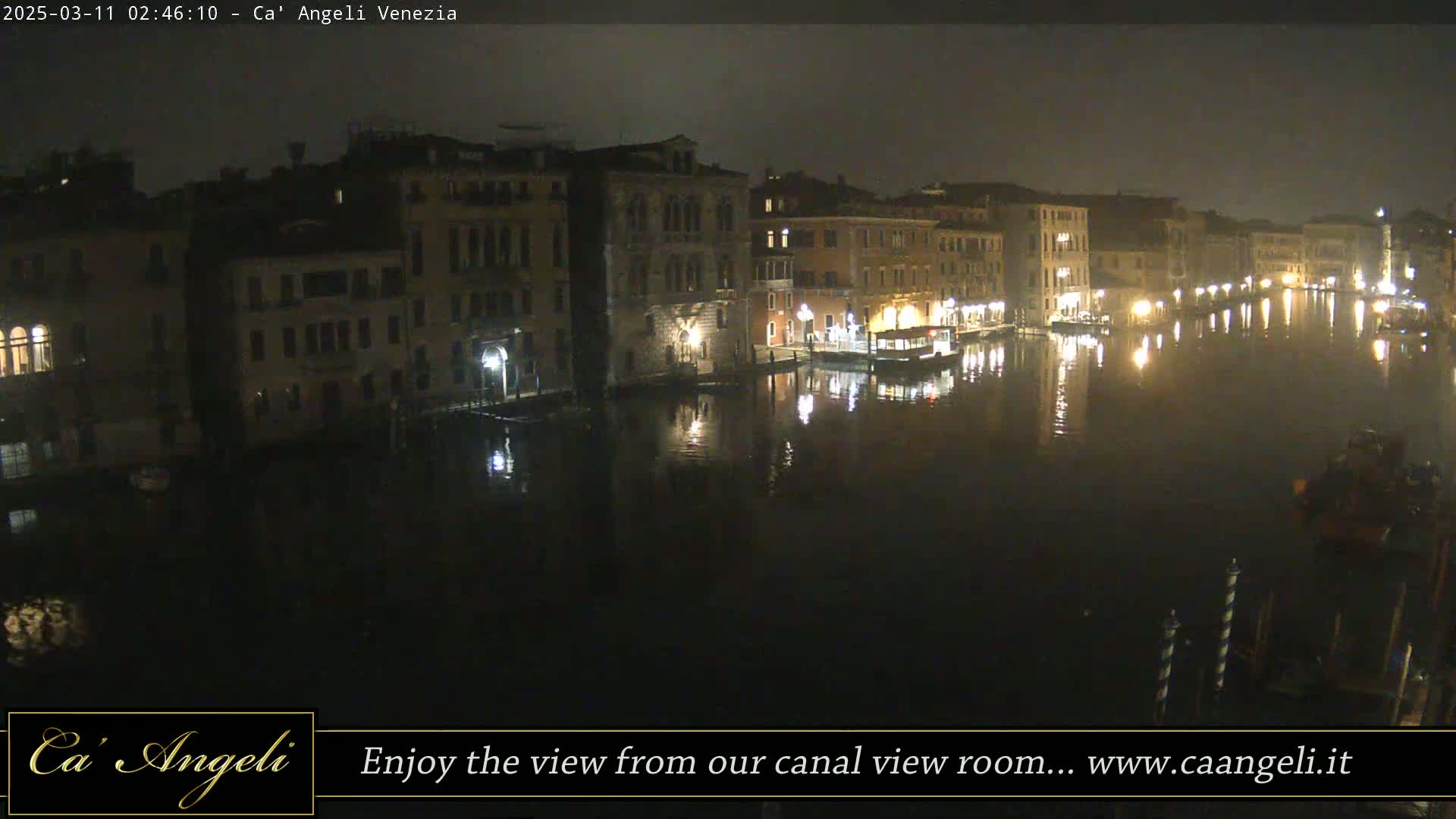 A nighttime view of a canal in Venice, with buildings lining the waterway and their lights reflecting on the calm water.
