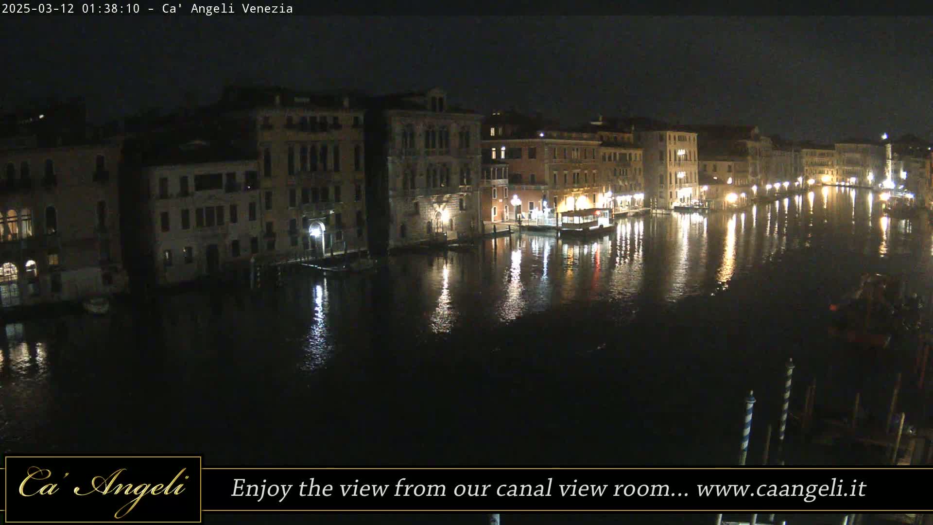 A nighttime view of a canal in Venice, Italy, shows buildings lit along the waterway, reflecting in the calm water.