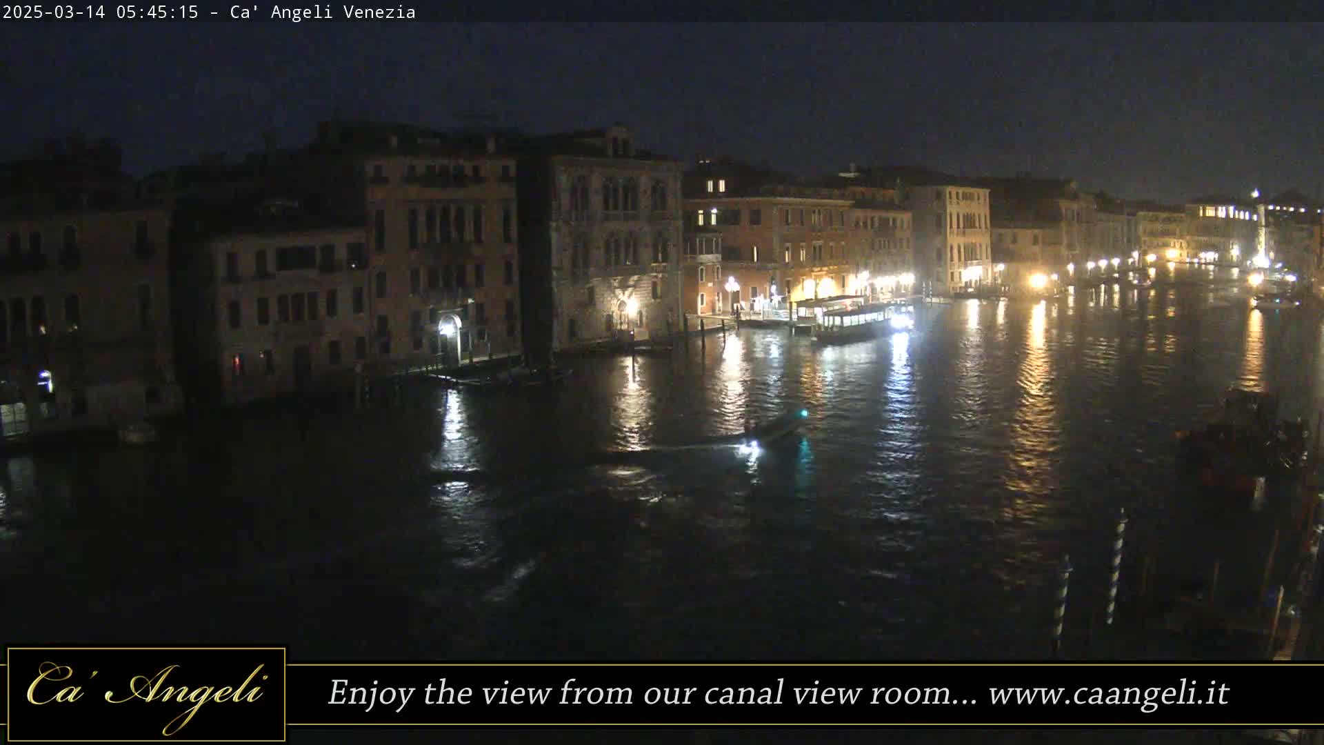 A nighttime view of a canal in Venice, with illuminated buildings lining its banks and several boats on the water.