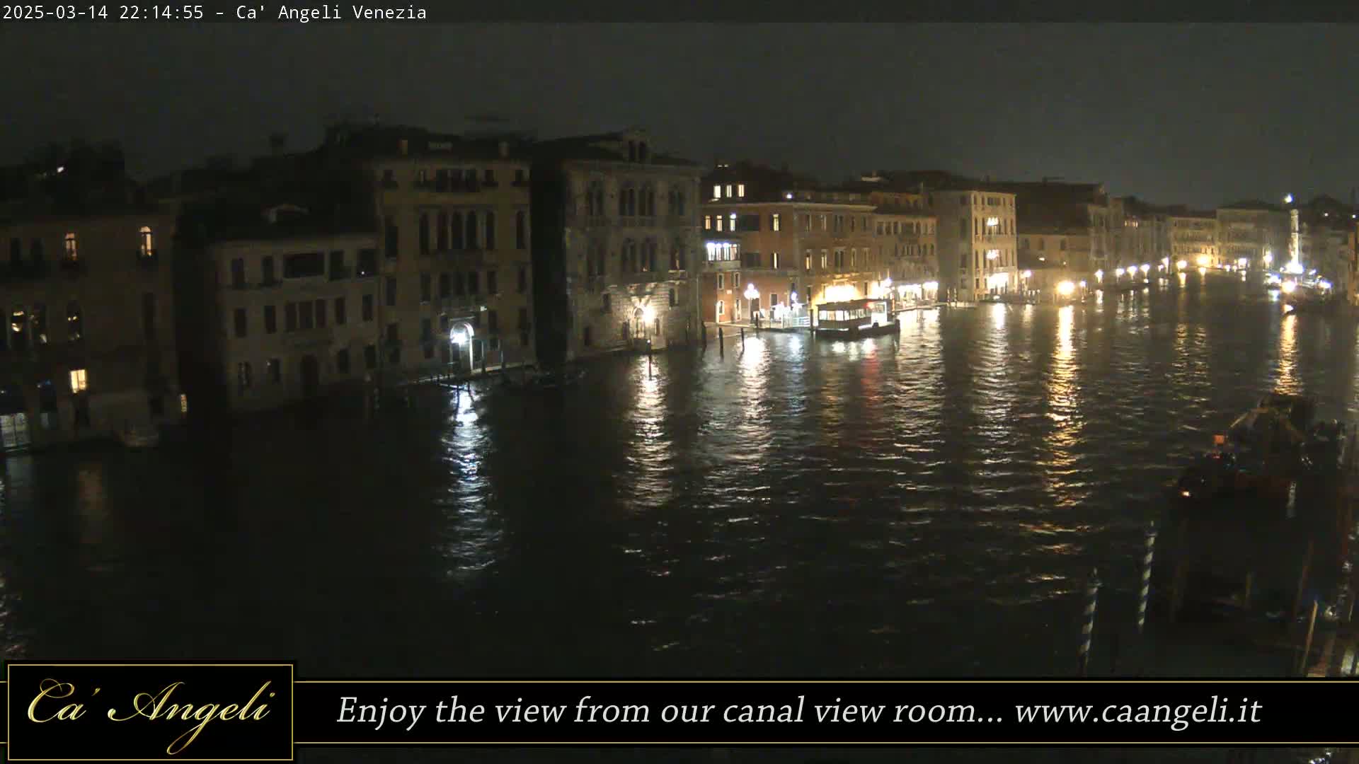 A nighttime view of a canal in Venice, with illuminated buildings lining the waterway and boats on the water.