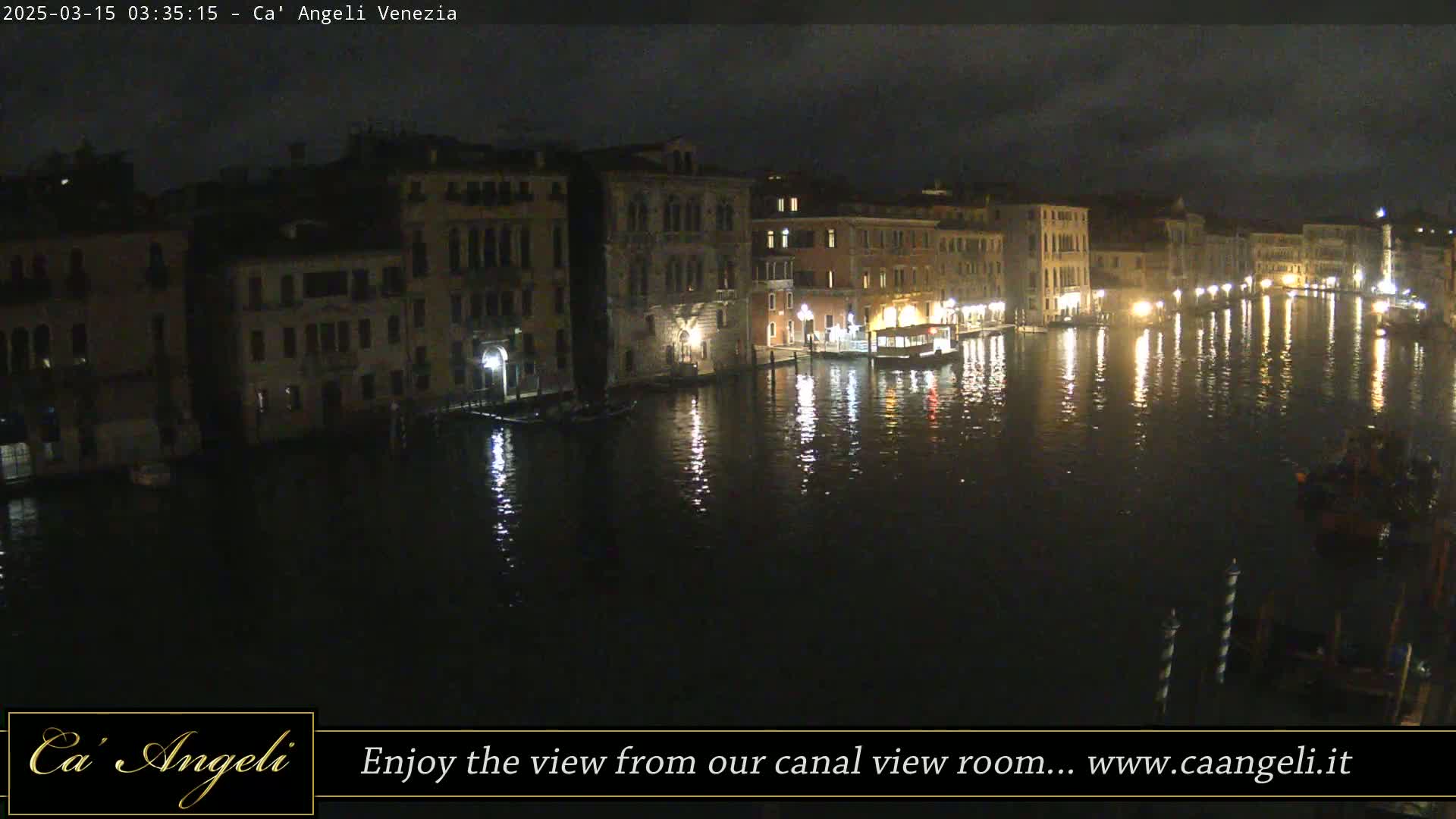 A nighttime view of a canal in Venice, with buildings lining both sides and their lights reflected in the dark water.