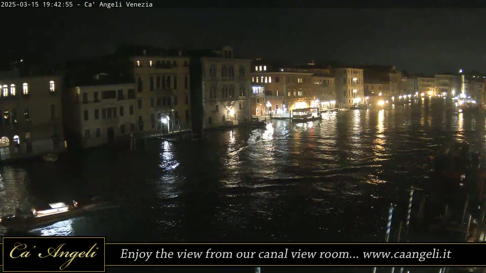 A nighttime view of a canal in Venice, with illuminated buildings lining the waterway and boats on the water.