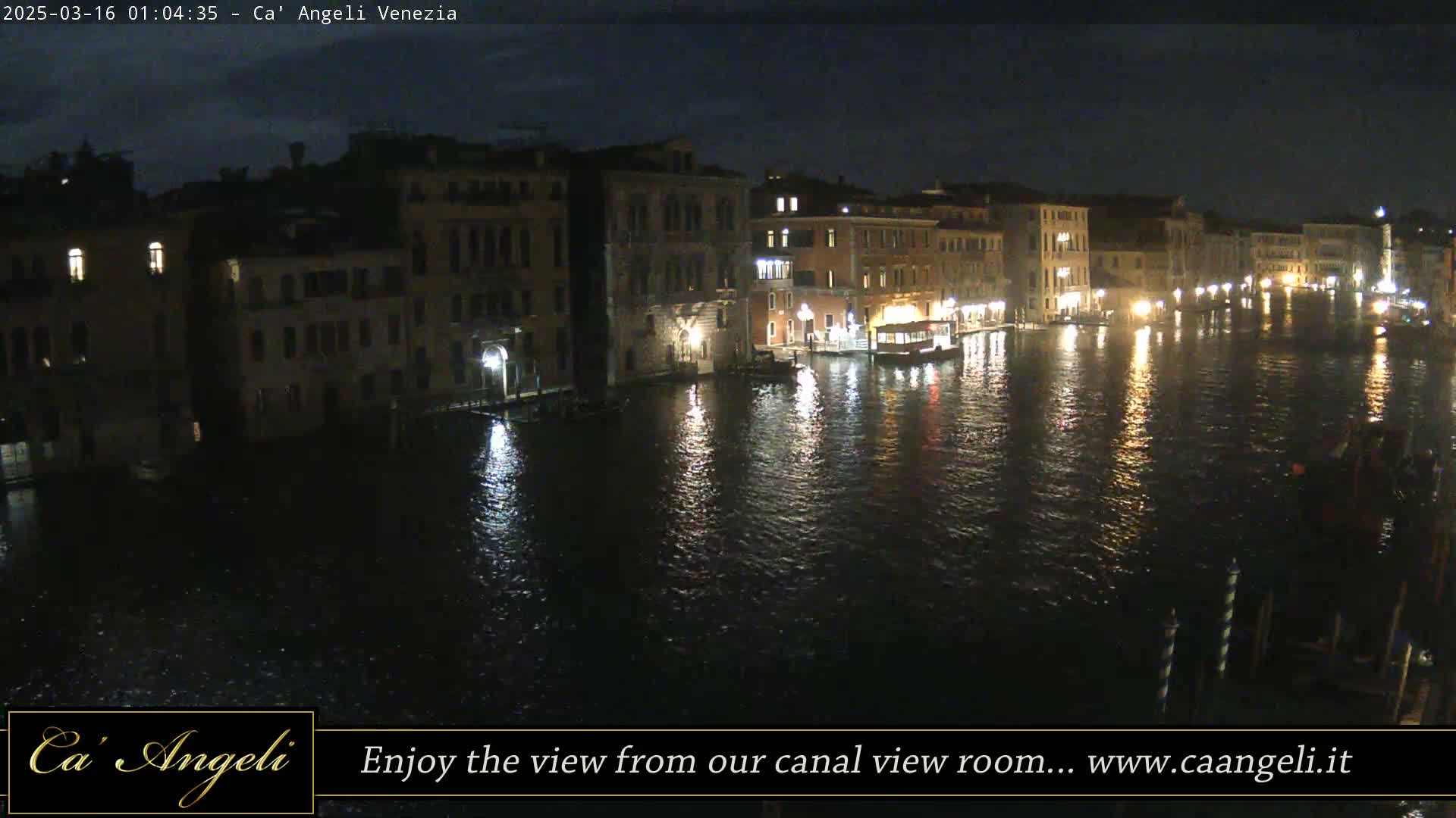 A nighttime view of a canal in Venice, with buildings lining both sides and their lights reflecting on the water.