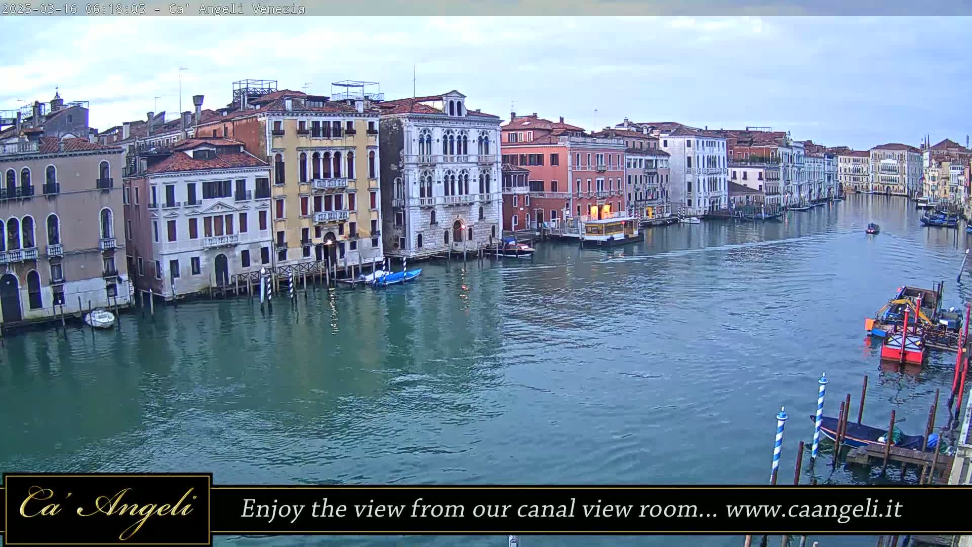 A wide shot of a calm canal in Venice, Italy, under an overcast sky, lined with historic buildings and a few small boats.