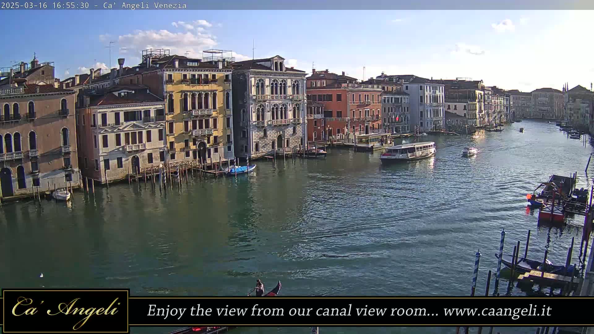 A sunny day in Venice shows a wide canal with colorful buildings lining the waterway, boats and gondolas are visible on the water.