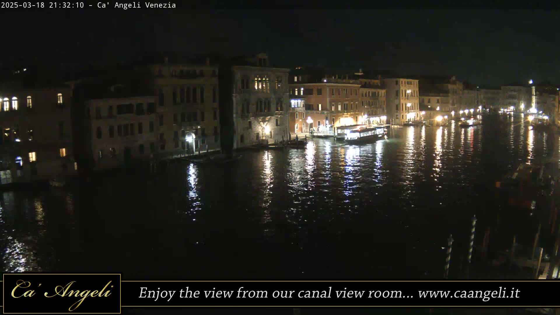 A nighttime view of a canal in Venice, Italy, with illuminated buildings lining the waterway and reflections shimmering on the water's surface.