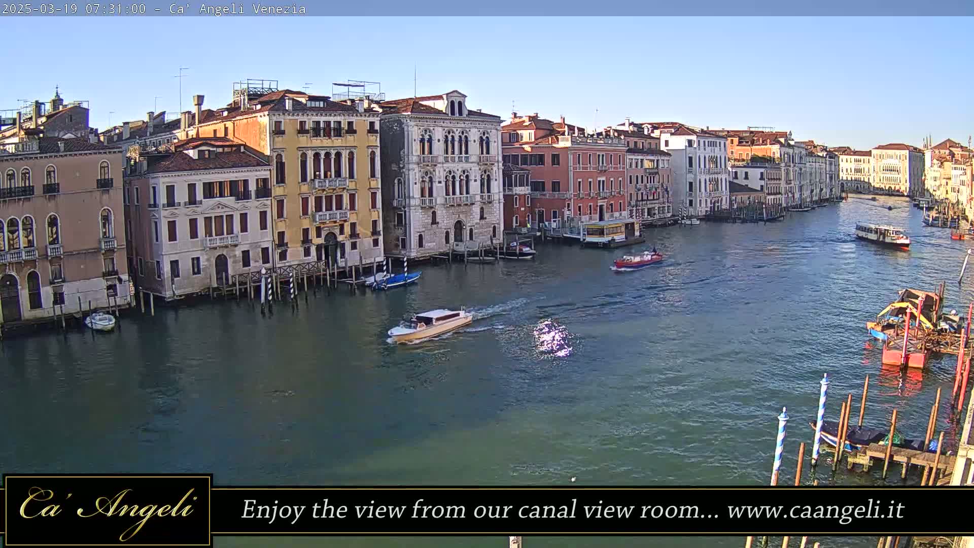 A sunny day in Venice shows a canal lined with tall, colorful buildings and several boats, including a water taxi.
