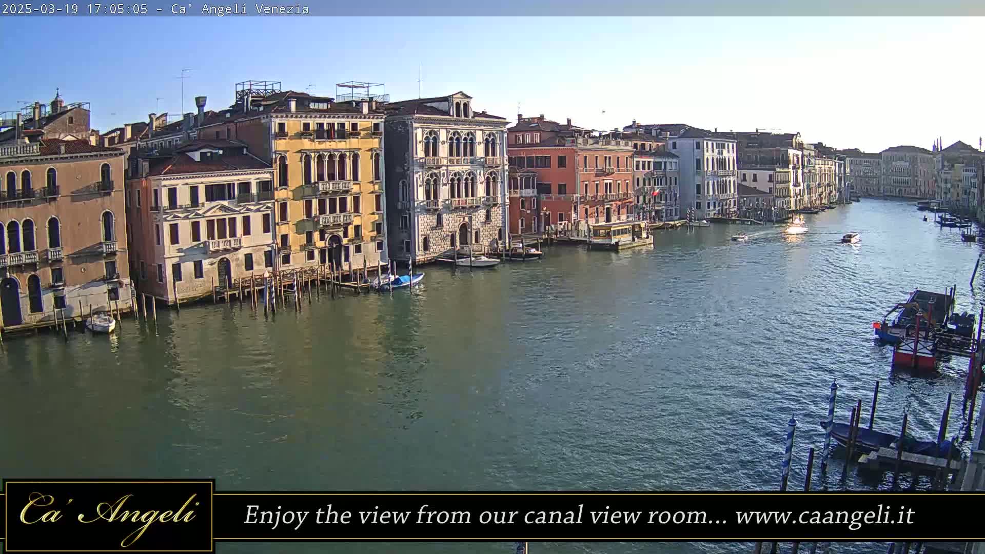 A sunny day in Venice shows a wide canal lined with several colorful buildings, some boats, and a barge.