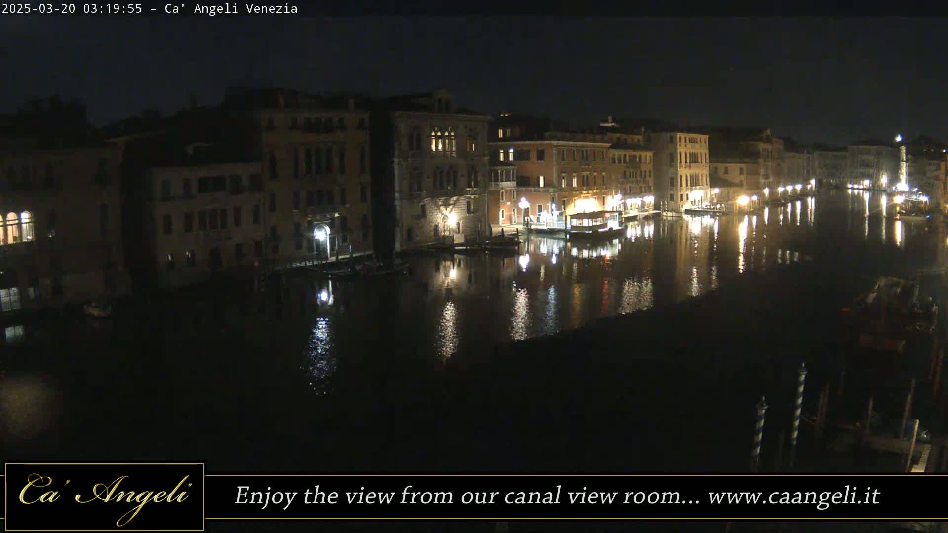 A nighttime view of a canal in Venice, lined with illuminated buildings, reflecting in the calm water.