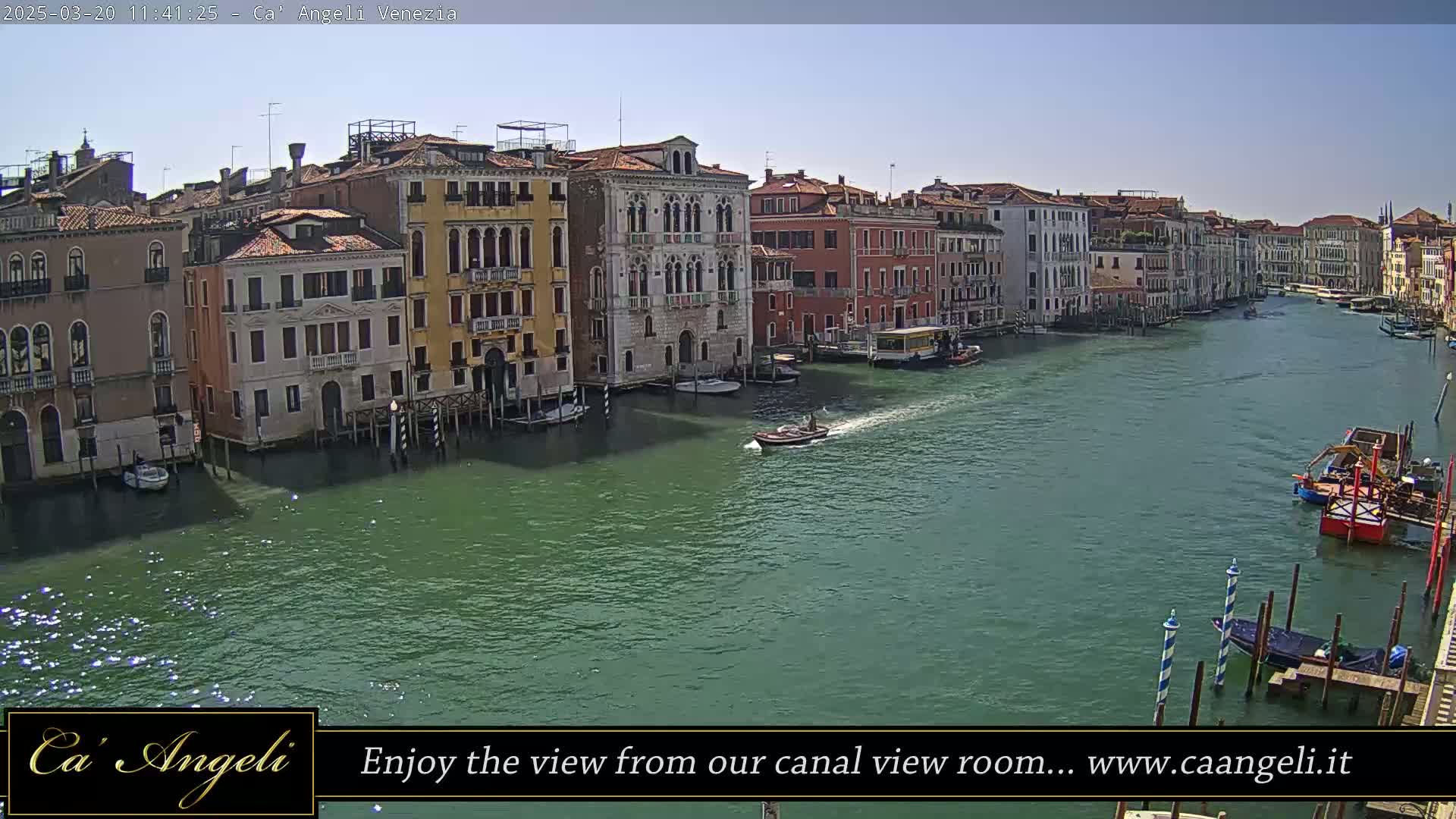 A sunny day shows a wide canal in Venice, Italy, lined with colorful buildings and a few boats on the water.
