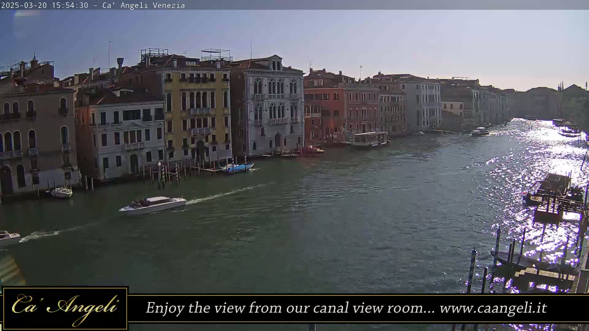 A sunny day in Venice shows a wide canal with several boats and buildings lining the waterway.