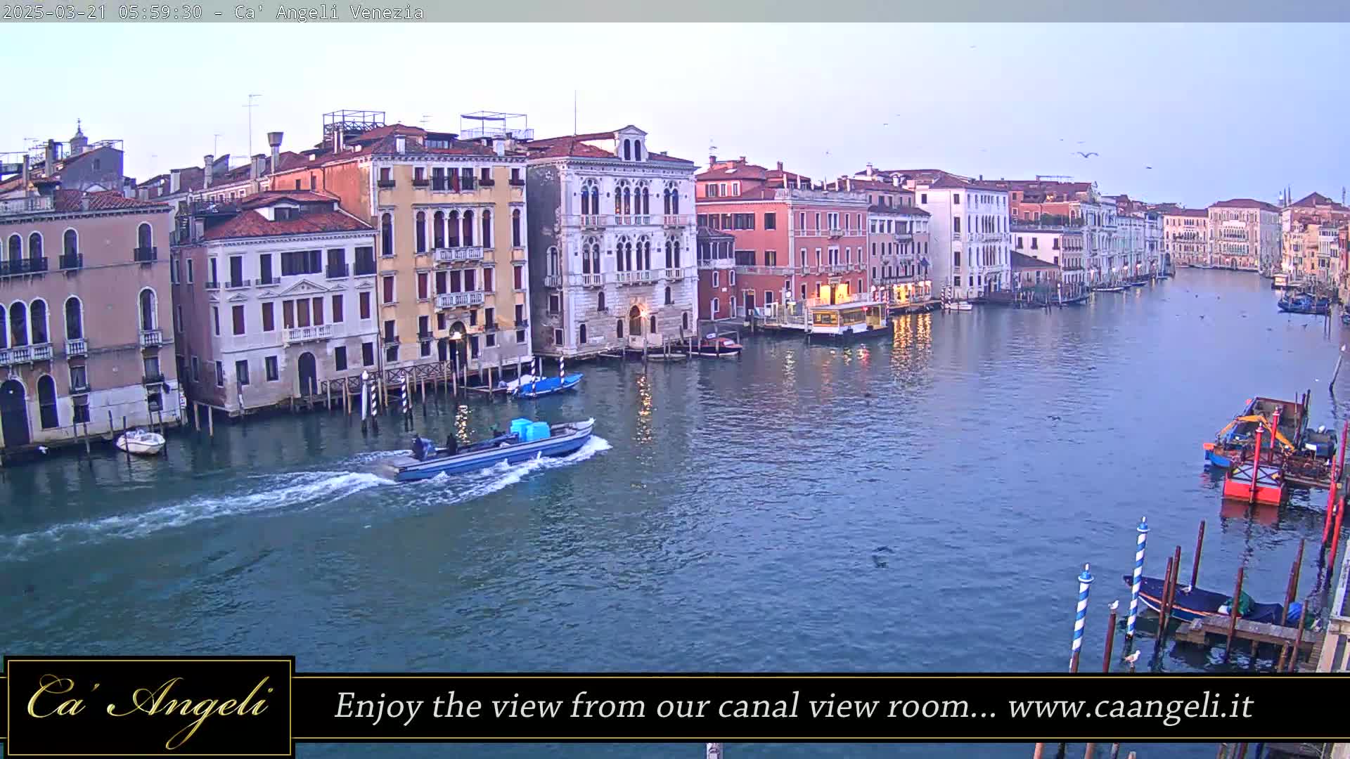 A wide canal in Venice, Italy, is seen at dawn, with several boats on the water and colorful buildings lining the banks.