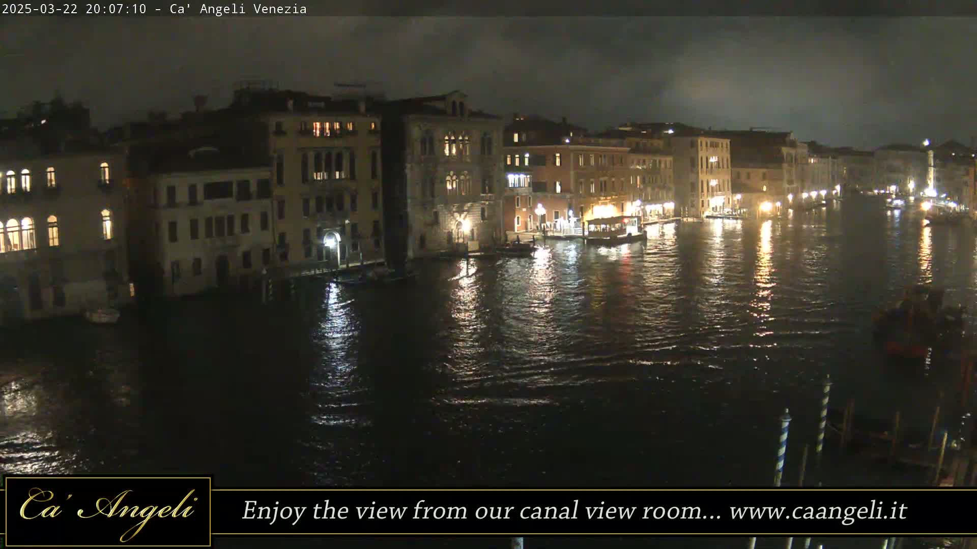 Nighttime view of a canal in Venice, Italy, with illuminated buildings lining the waterway under a partly cloudy sky.