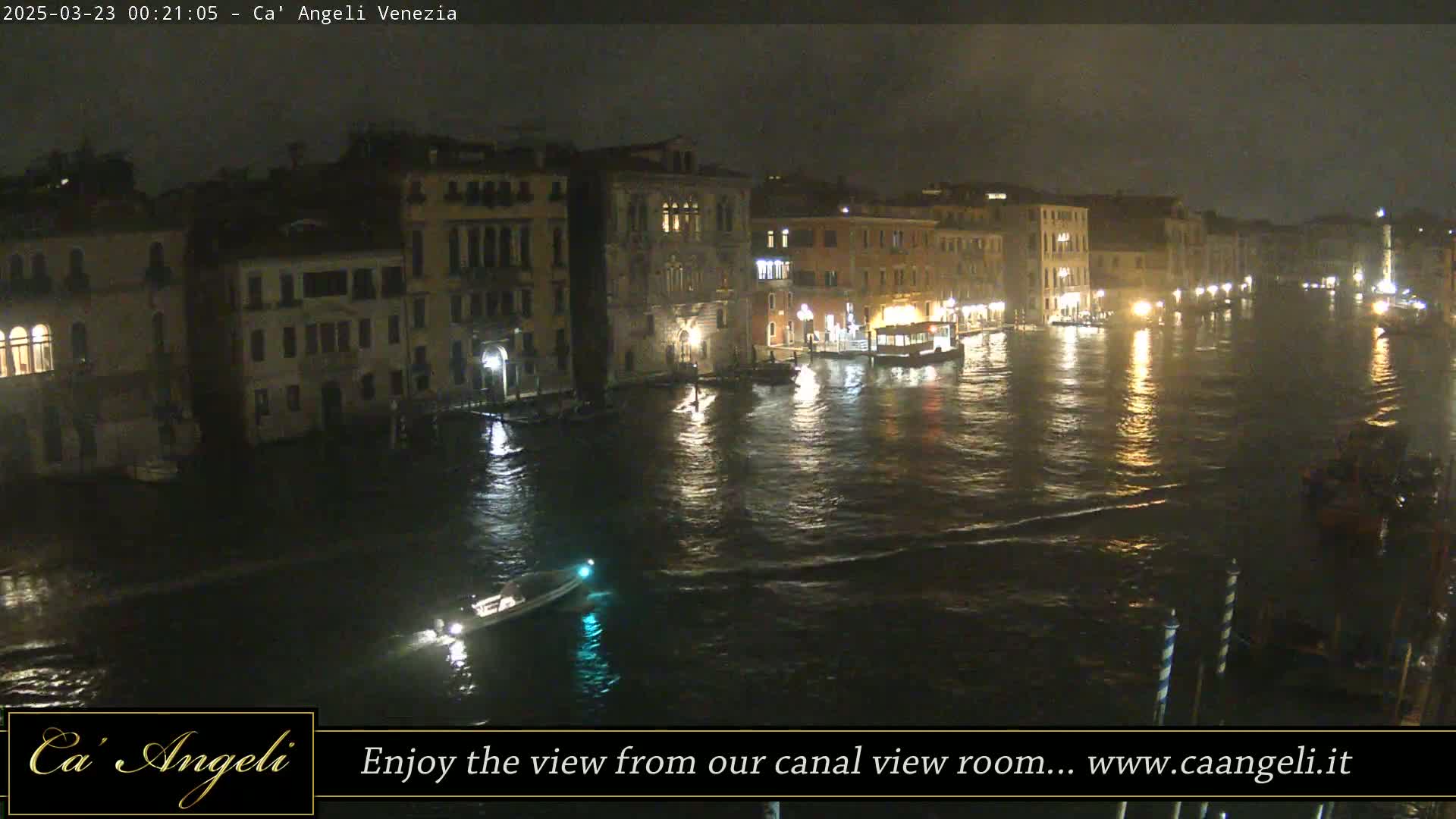 A nighttime view of a canal in Venice, showing buildings along the waterfront and boats on the water.