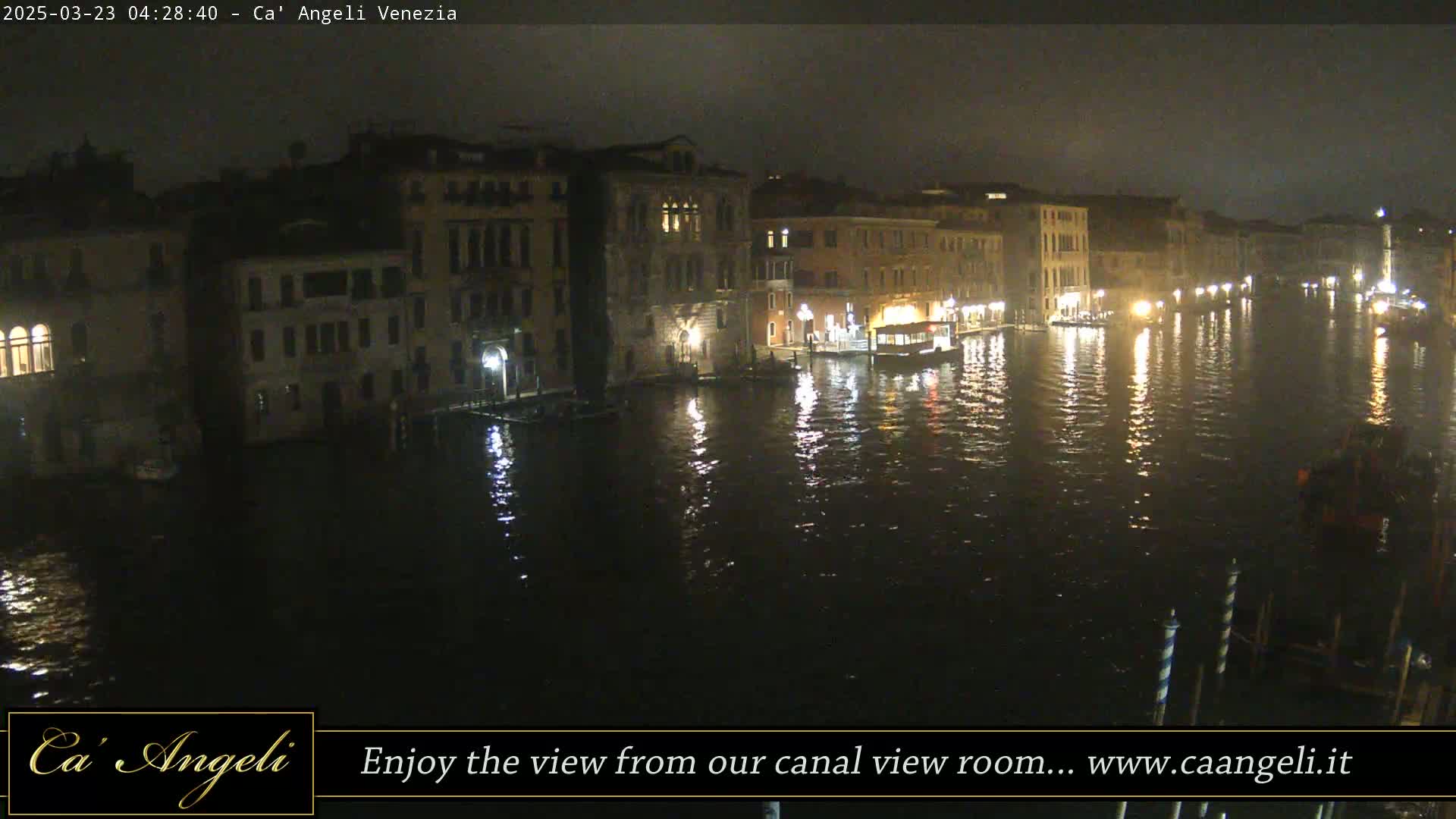 A nighttime view of a canal in Venice, with illuminated buildings lining its banks and the water reflecting the city lights.