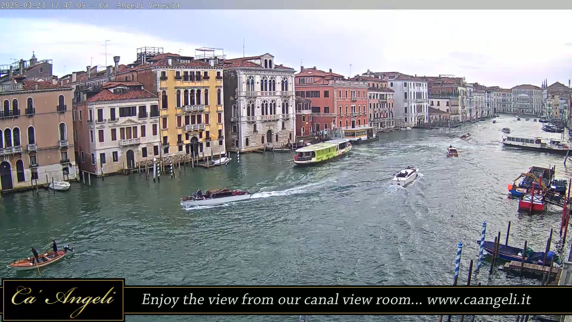 A waterway lined with buildings in Venice is shown on an overcast day, with several boats moving along the water.
