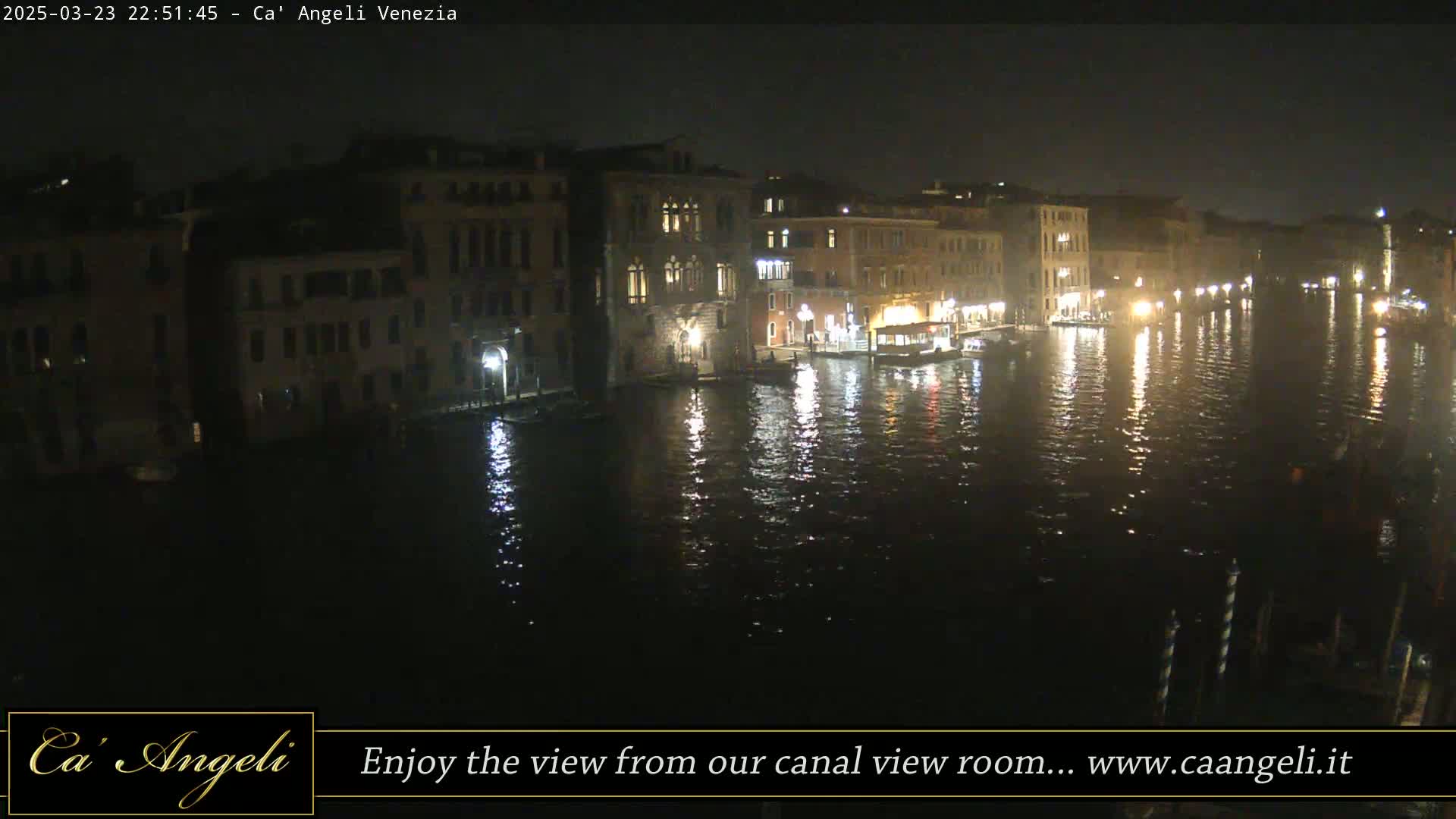A nighttime view of a canal in Venice, showing illuminated buildings reflected in the dark water.