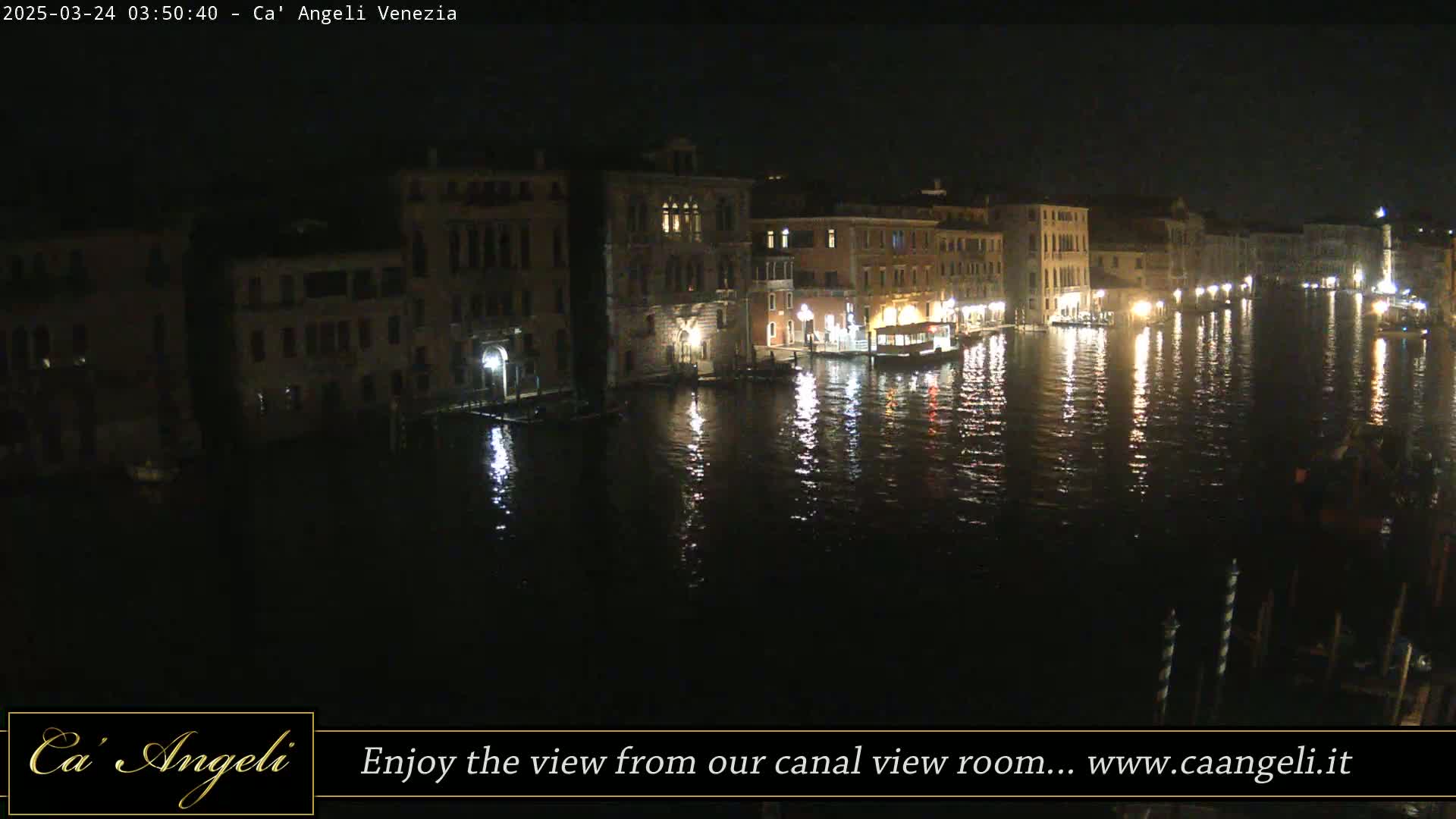 Dark, illuminated buildings line a calm canal at night, their lights reflecting on the water.