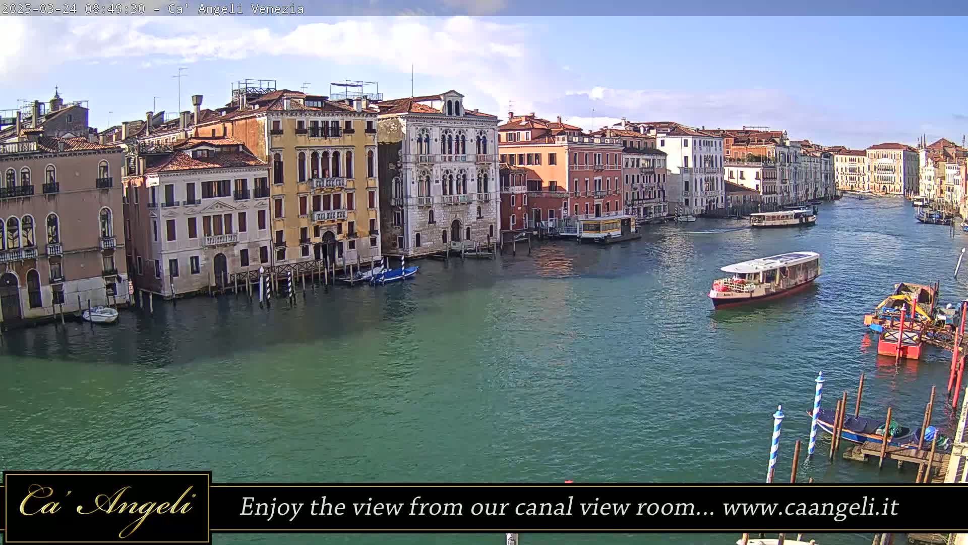 A sunny day in Venice shows a wide canal with several boats and numerous buildings lining the waterway.