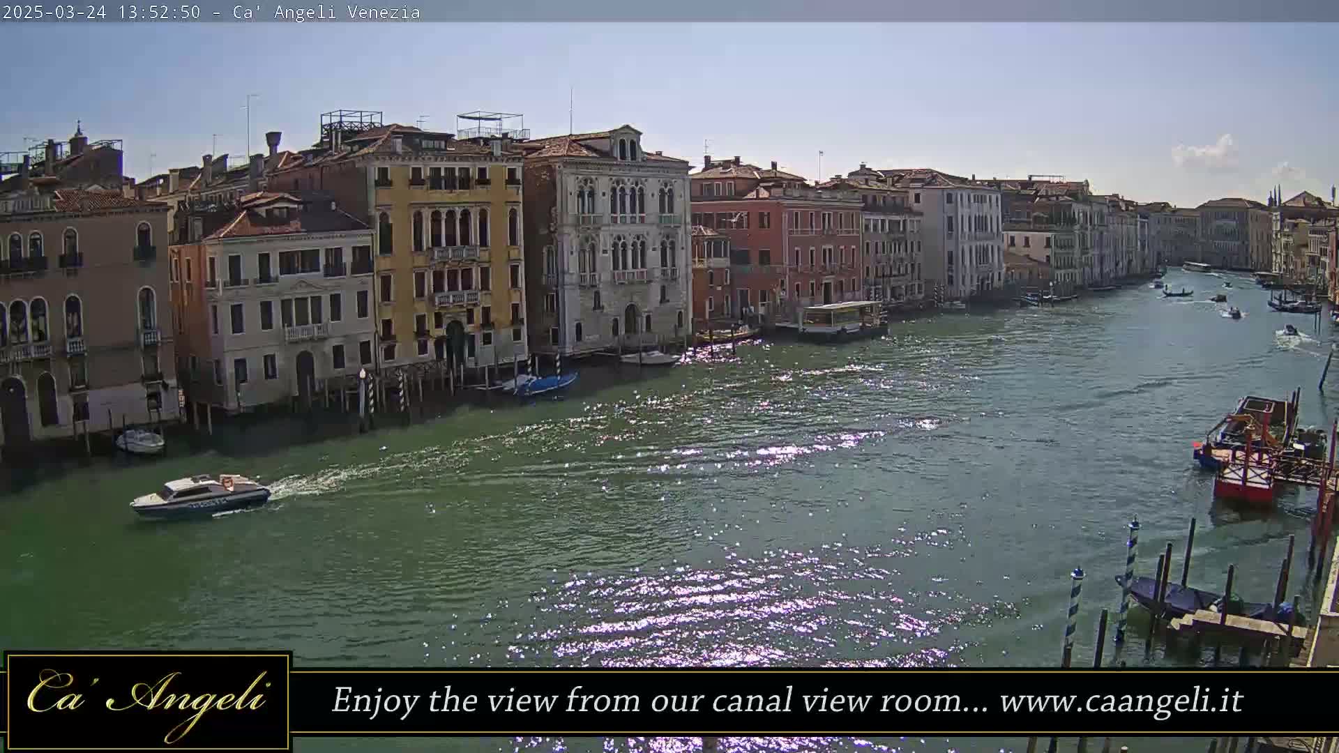 A sunny day in Venice shows a wide canal with several boats and buildings lining the waterway.