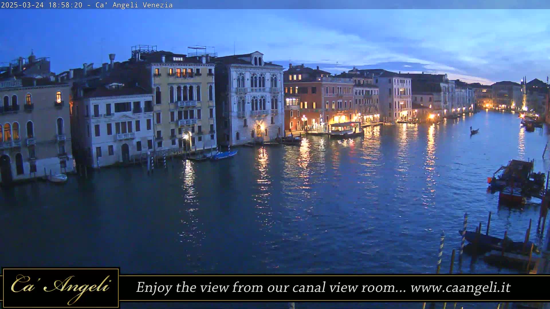 A twilight view of a Venetian canal lined with illuminated buildings, with several boats moored along the waterway.