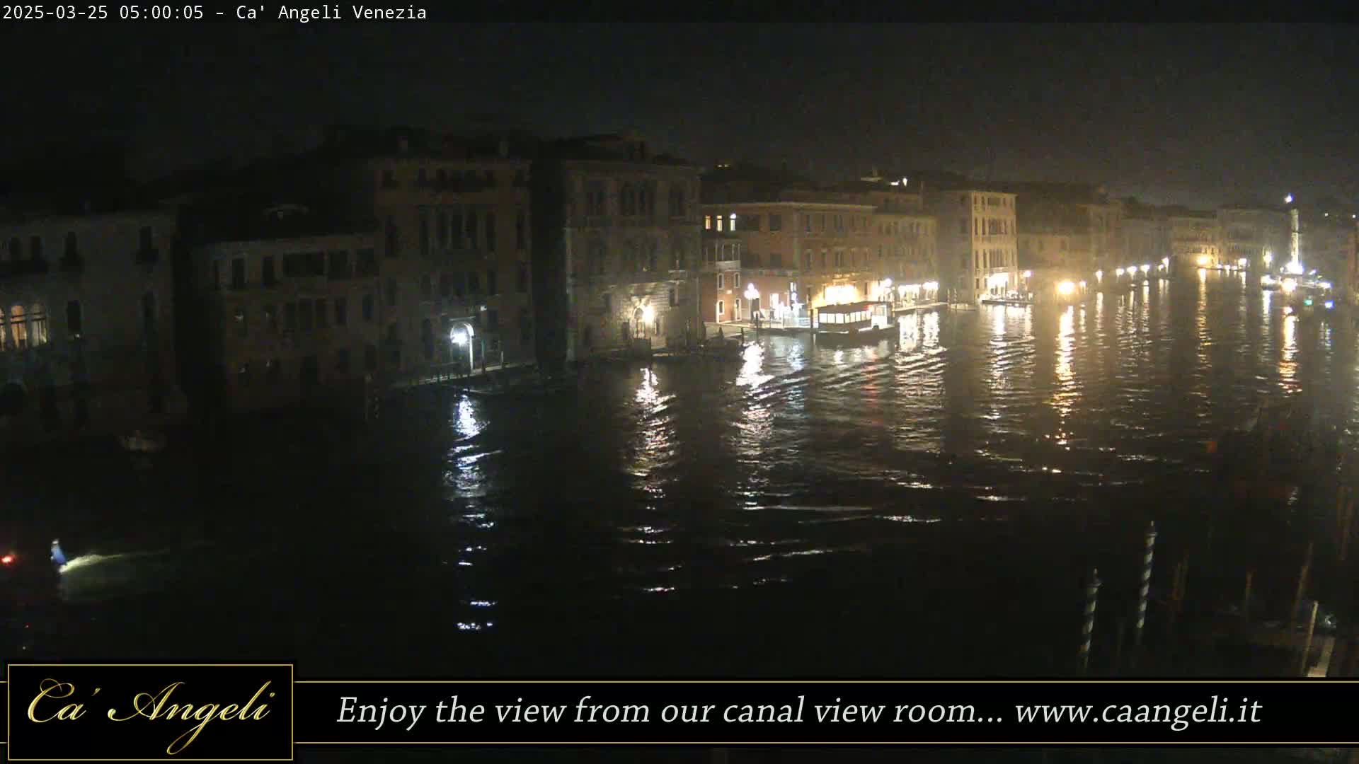 A nighttime view of a canal in Venice, with buildings lining both sides and lights reflecting on the water.