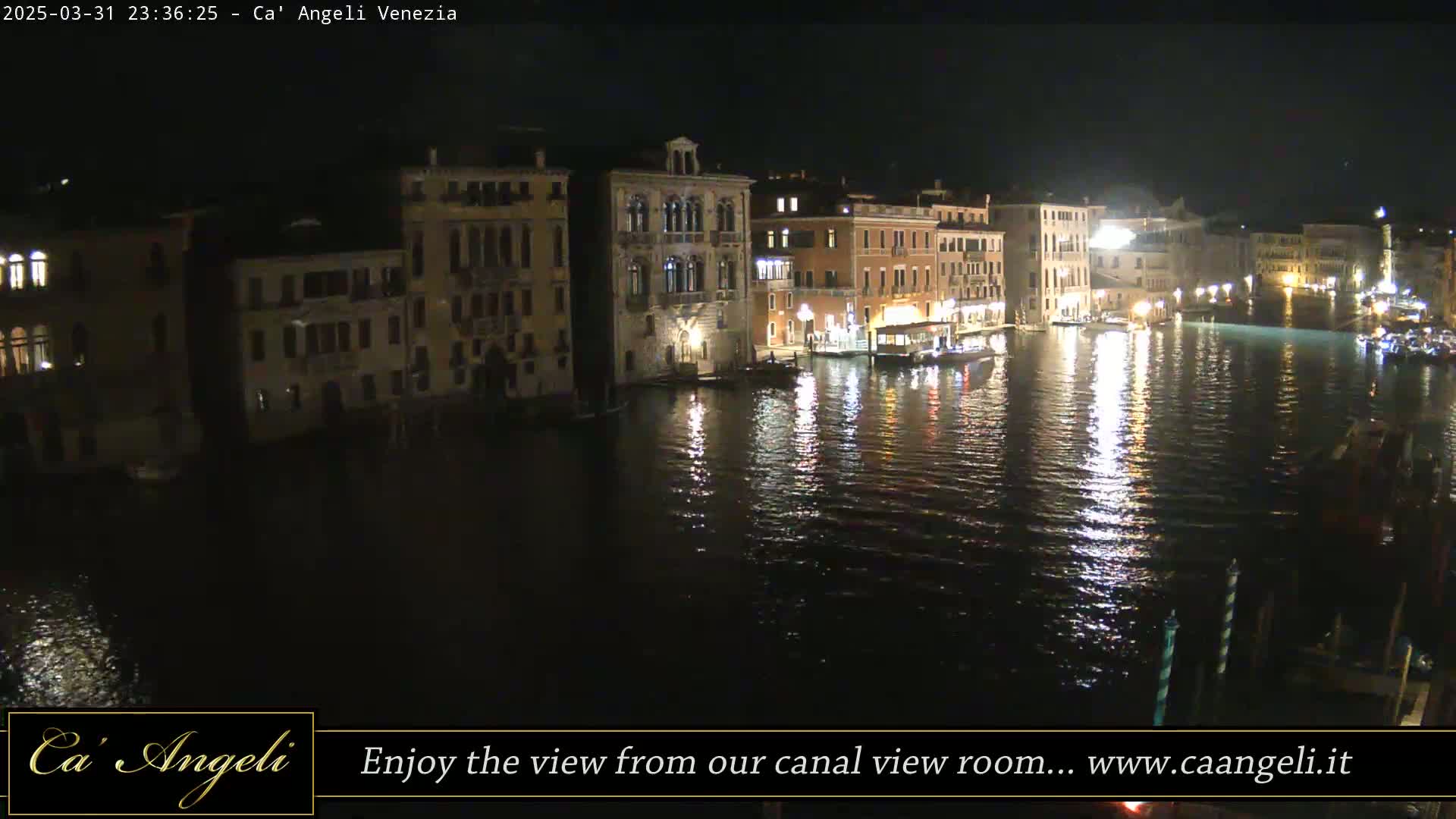 A nighttime view of a canal in Venice, with illuminated buildings lining the waterway and their lights reflecting on the calm water.