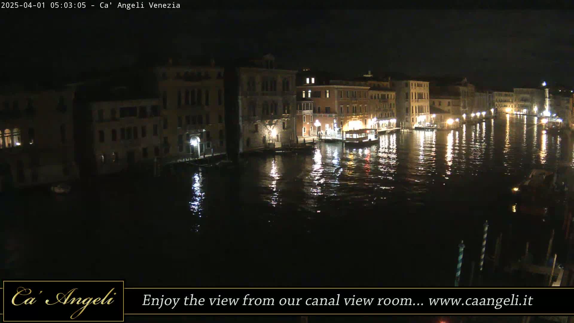 Nighttime view of a canal in Venice, with illuminated buildings lining the waterway and their lights reflecting on the dark water.