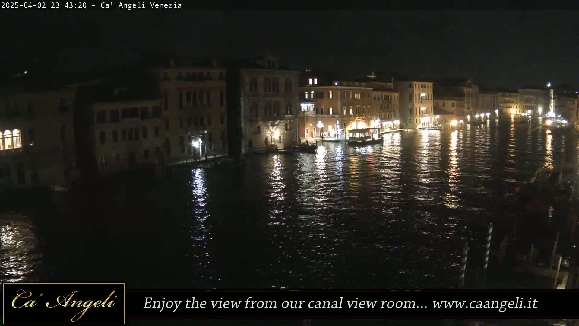 A nighttime view of a canal in Venice, with illuminated buildings lining its banks and their reflections shimmering on the dark water.
