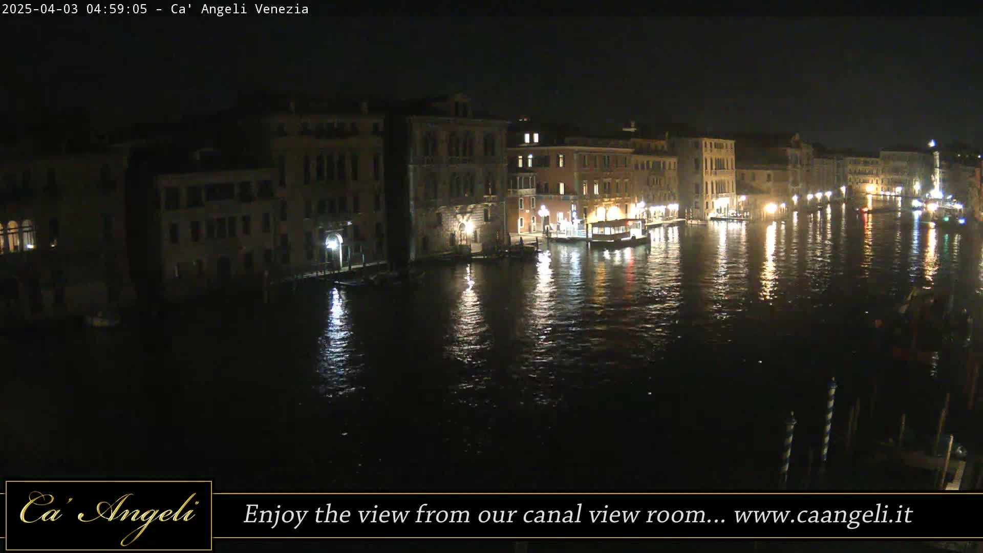 A nighttime view of a canal in Venice, Italy, shows buildings lining the waterway, reflecting lights on the dark water.