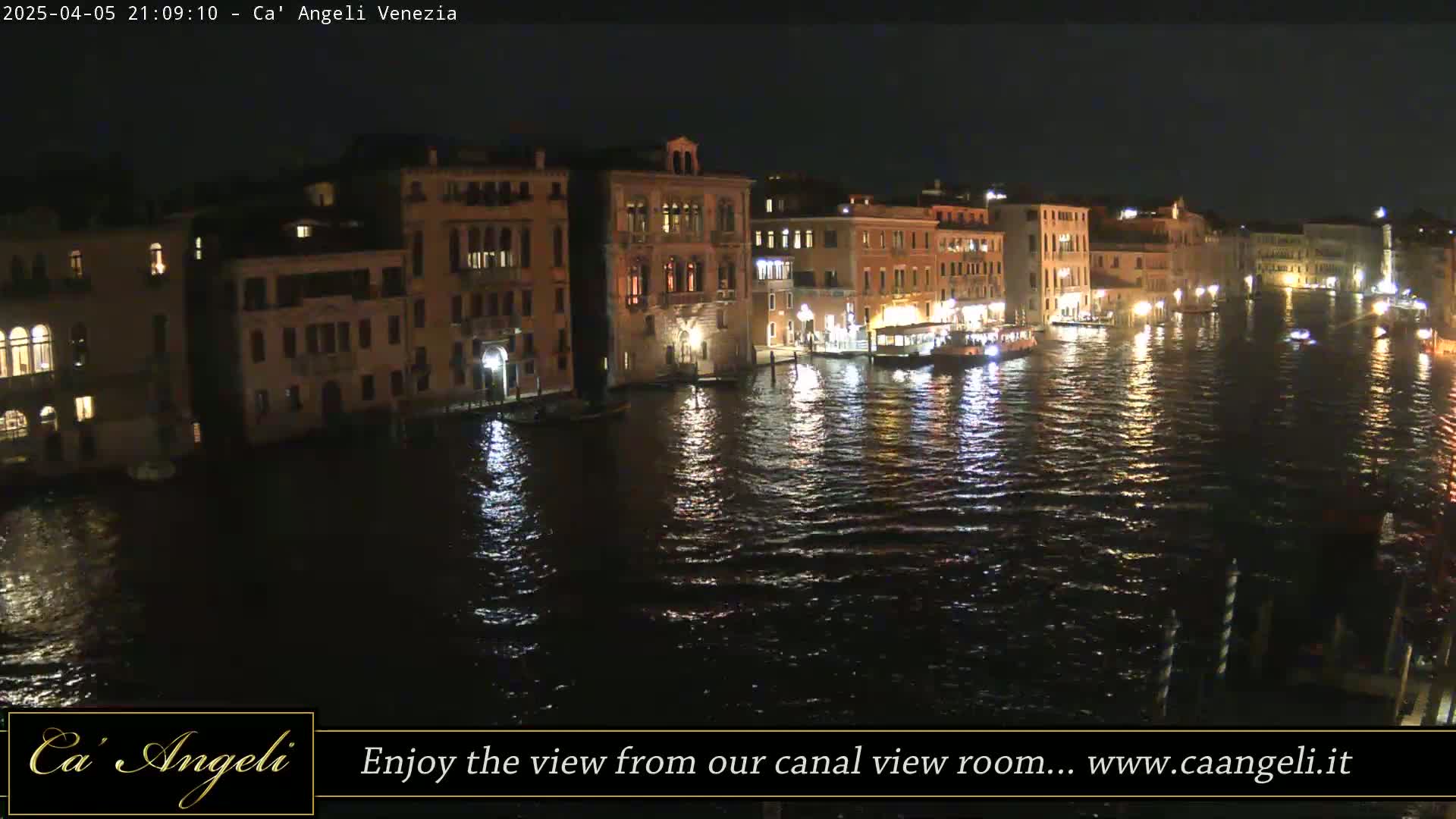 A nighttime view of illuminated buildings lining a canal, with boats on the water.