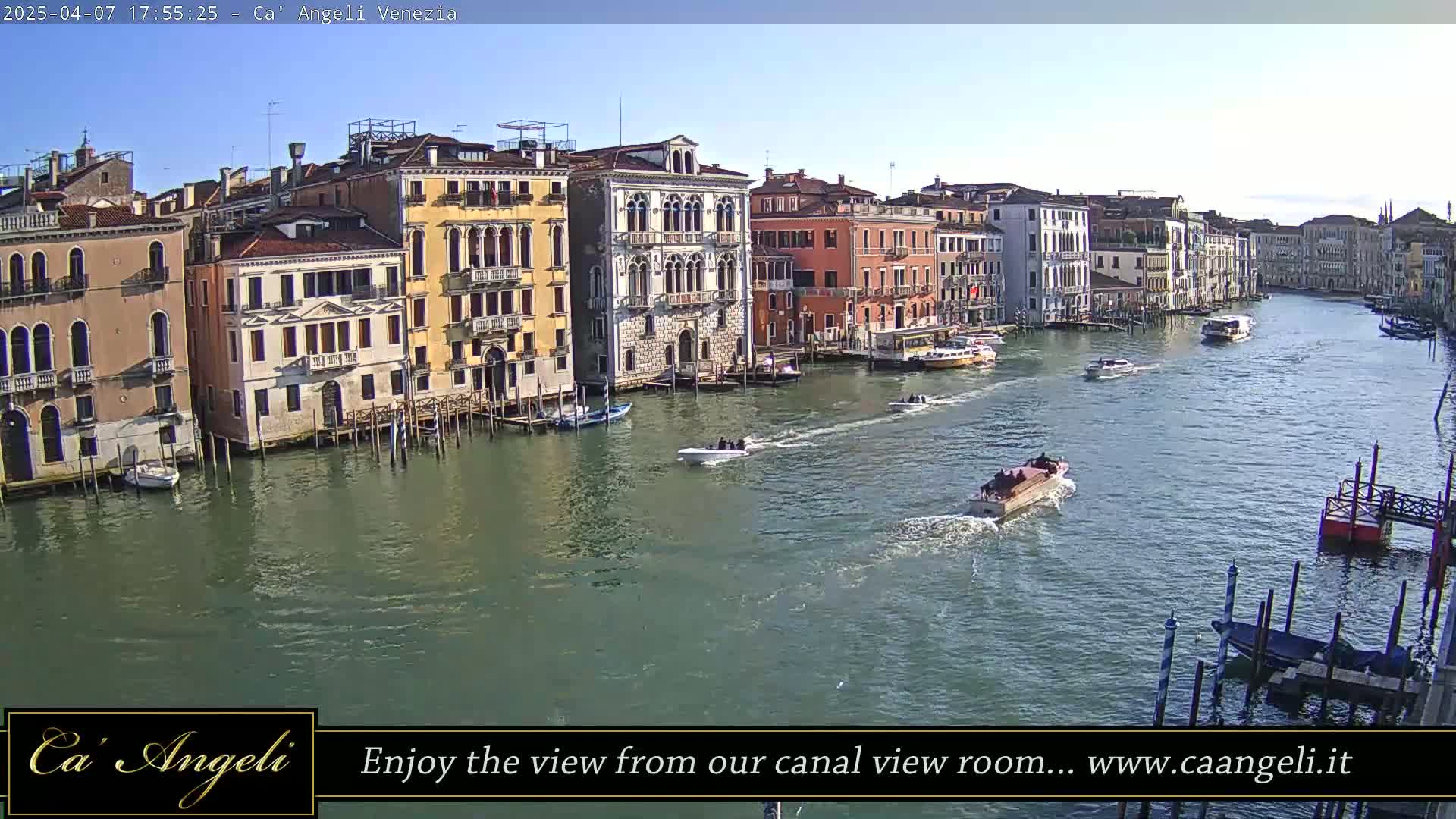 A sunny day in Venice shows a wide canal with several boats and colorful buildings lining the waterway.