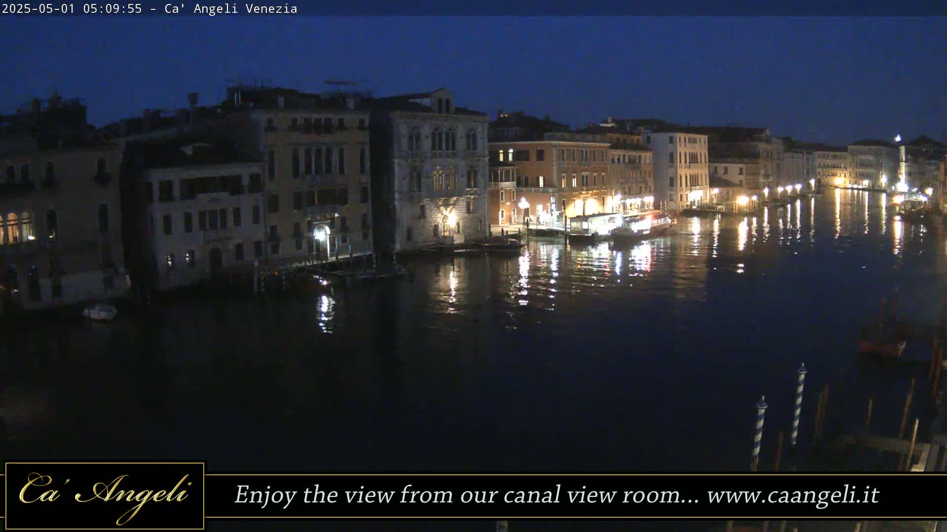 A nighttime view of a canal in Venice, with illuminated buildings lining the waterway and their lights reflecting on the dark water.