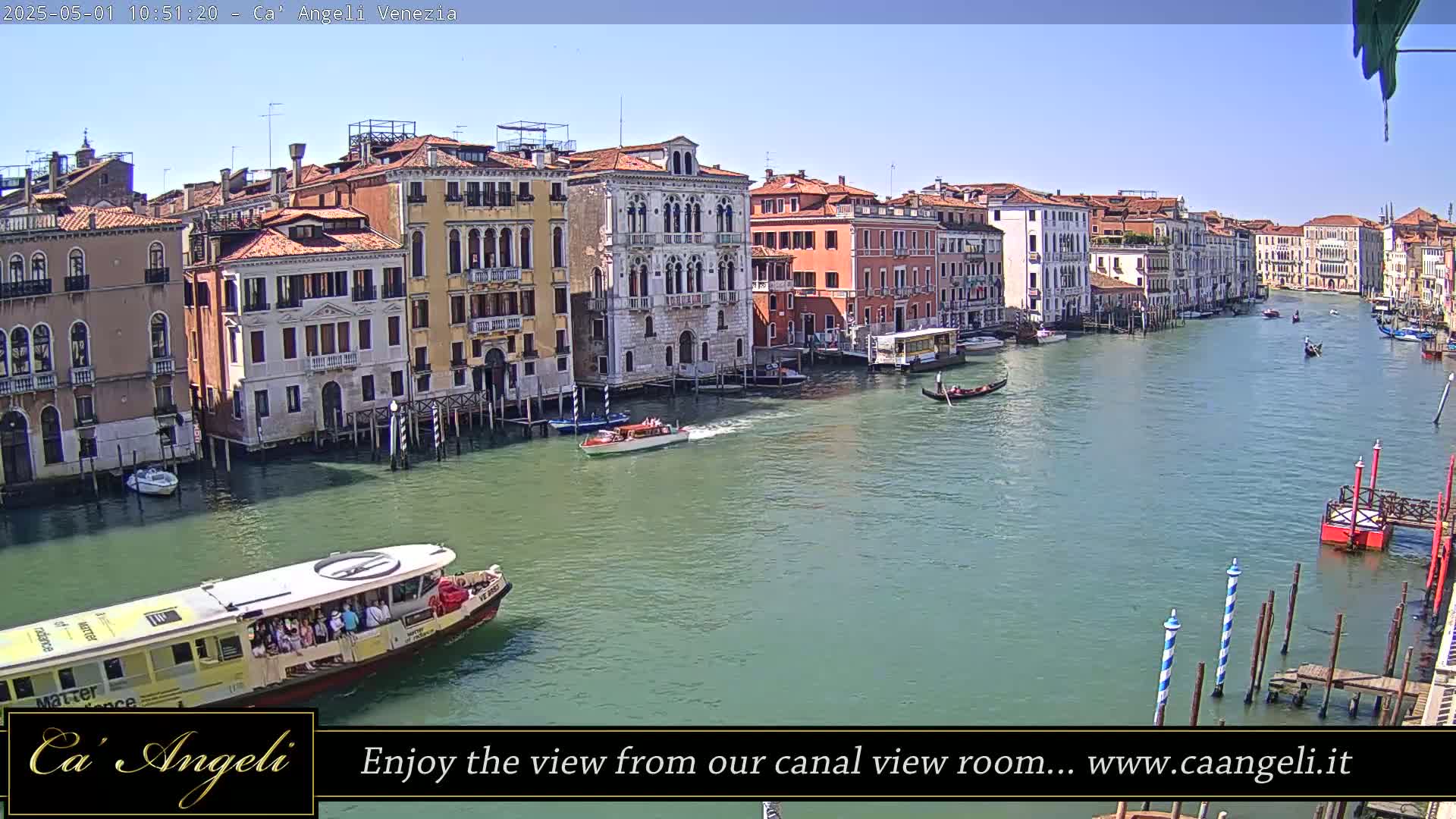 A sunny day shows a wide canal in Venice, Italy, lined with colorful buildings, with boats and gondolas traveling along the waterway.