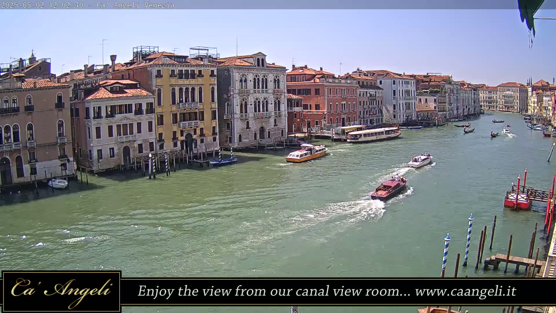 A sunny day in Venice shows a canal filled with boats passing by colorful buildings.