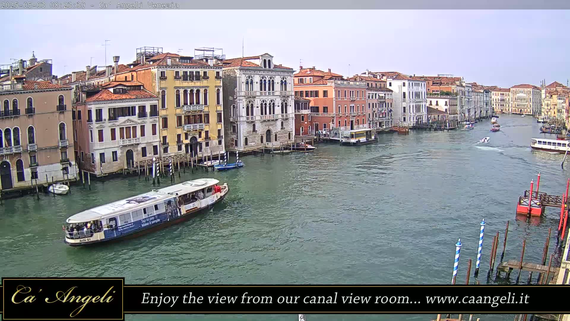 A waterway, under a mostly clear sky, is lined with tall, colorful buildings, and several boats are on the water.
