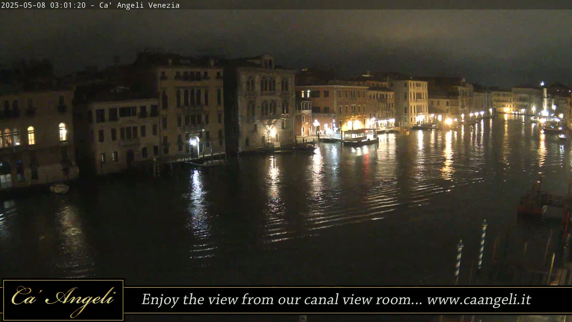A nighttime view of a canal in Venice, with illuminated buildings lining the waterway and their lights reflecting on the water.