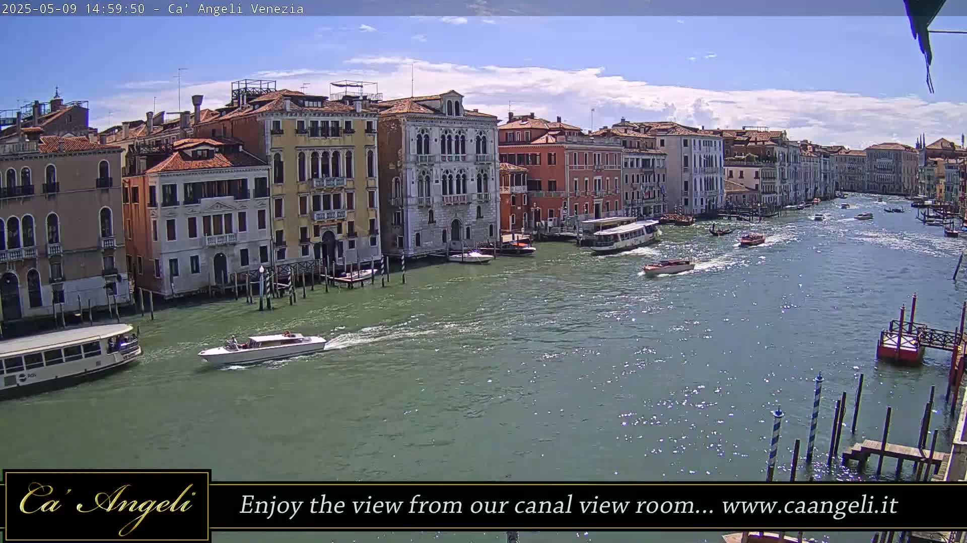 A sunny day in Venice shows a wide canal with several boats and buildings lining the waterway.