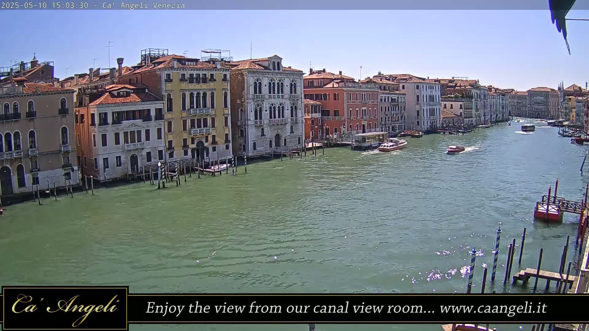 A sunny day in Venice shows a wide canal with several boats, lined by tall buildings with colorful facades.