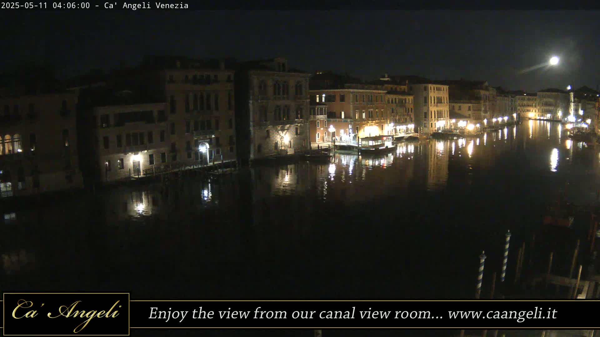A moonlit nighttime view of a canal in Venice, showing buildings lining the waterway with their lights reflected in the water.