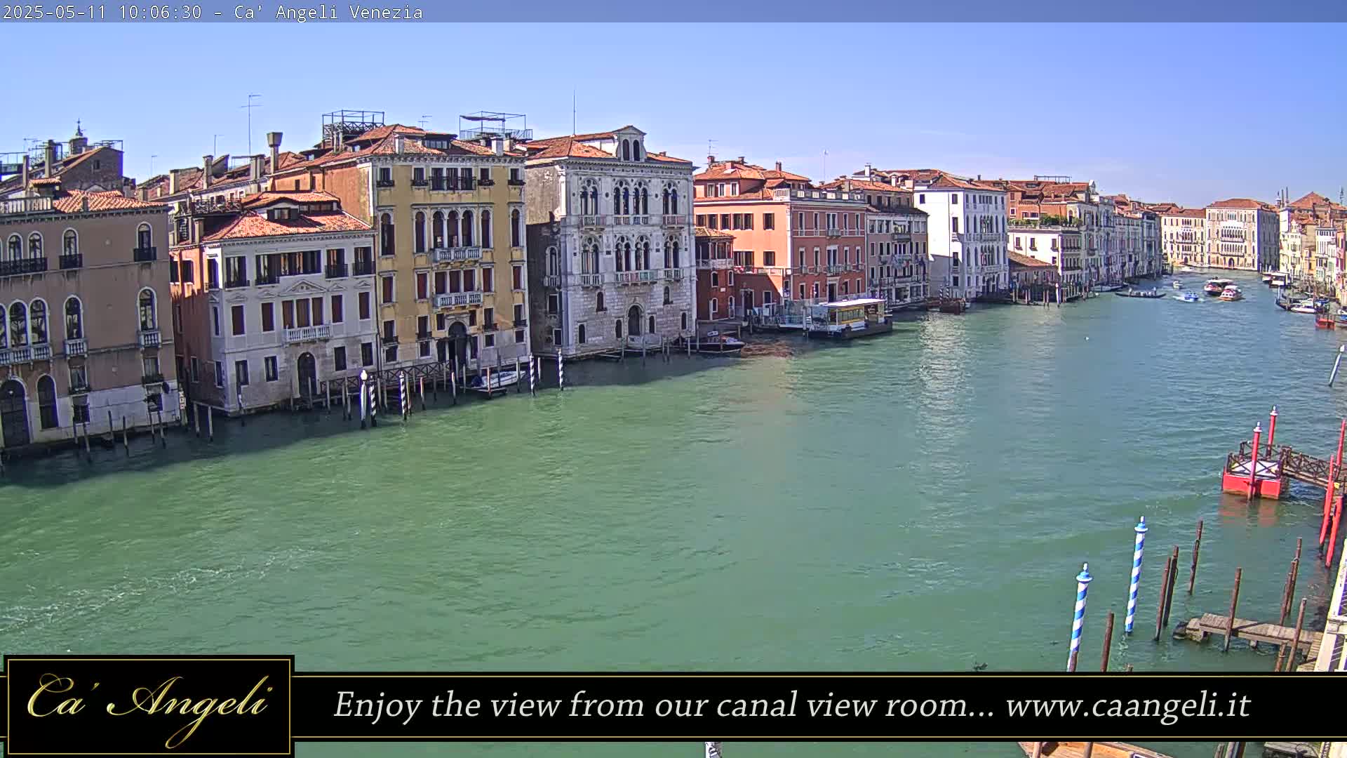 A sunny view of a canal in Venice, Italy, shows several buildings lining the waterway, with boats on the green water.